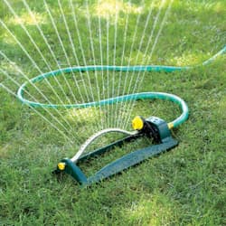 A lawn sprinkler with a hose attached to it is spraying water on a lush green lawn.