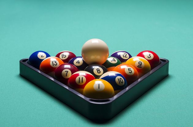 Billiard balls racked in a black triangle on a teal table, with the cue ball at the front.