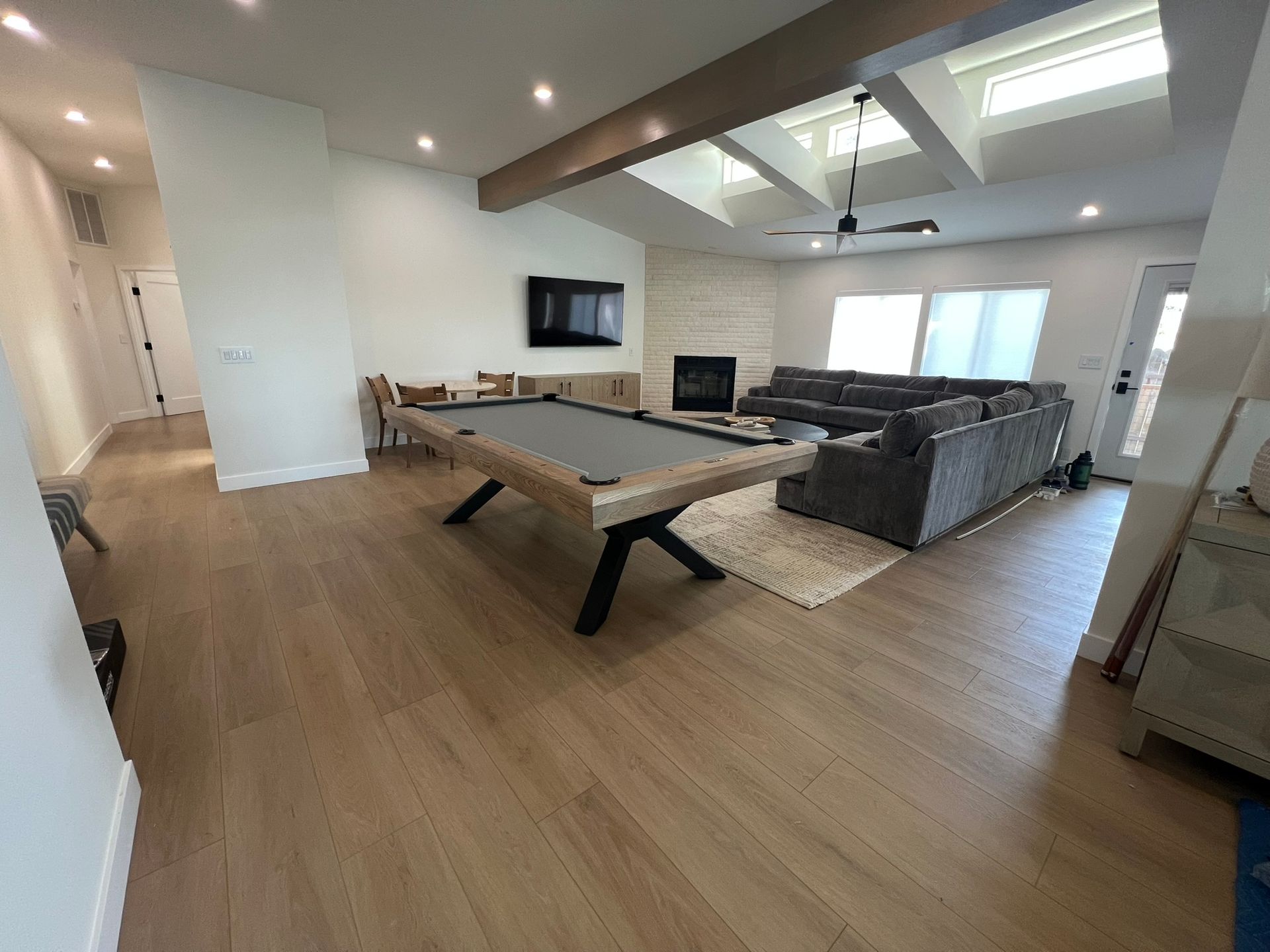 Spacious living room with pool table, sectional sofa, TV, and large windows on wood floors