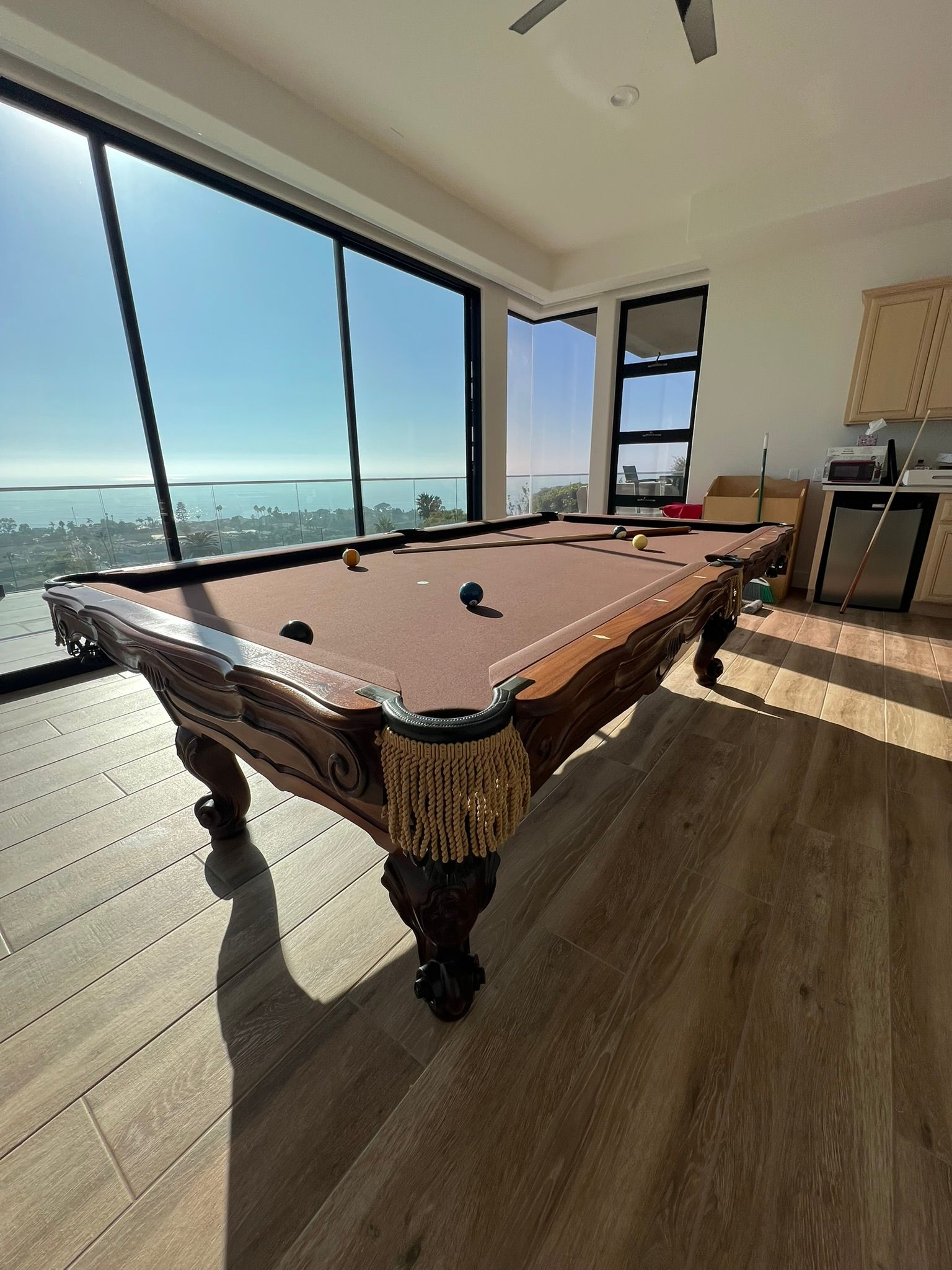 Spacious pool room with a pool table by floor-to-ceiling windows overlooking a city view.
