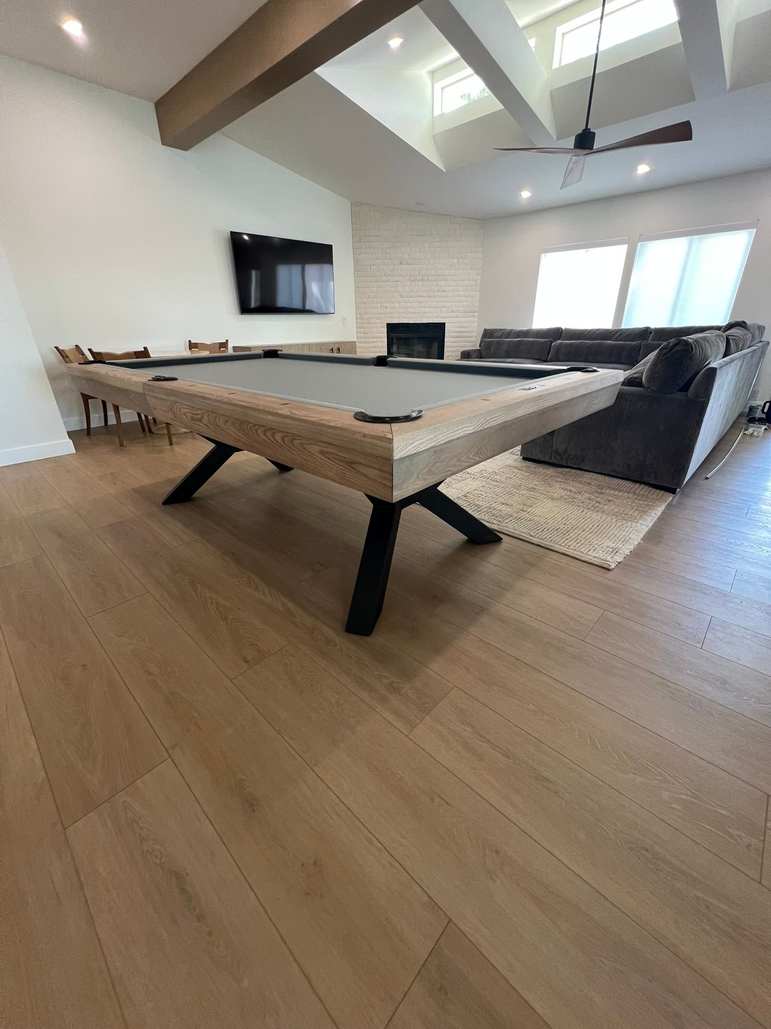 Modern living room with pool table, sectional sofa, fireplace, and wall-mounted TV under high ceilings