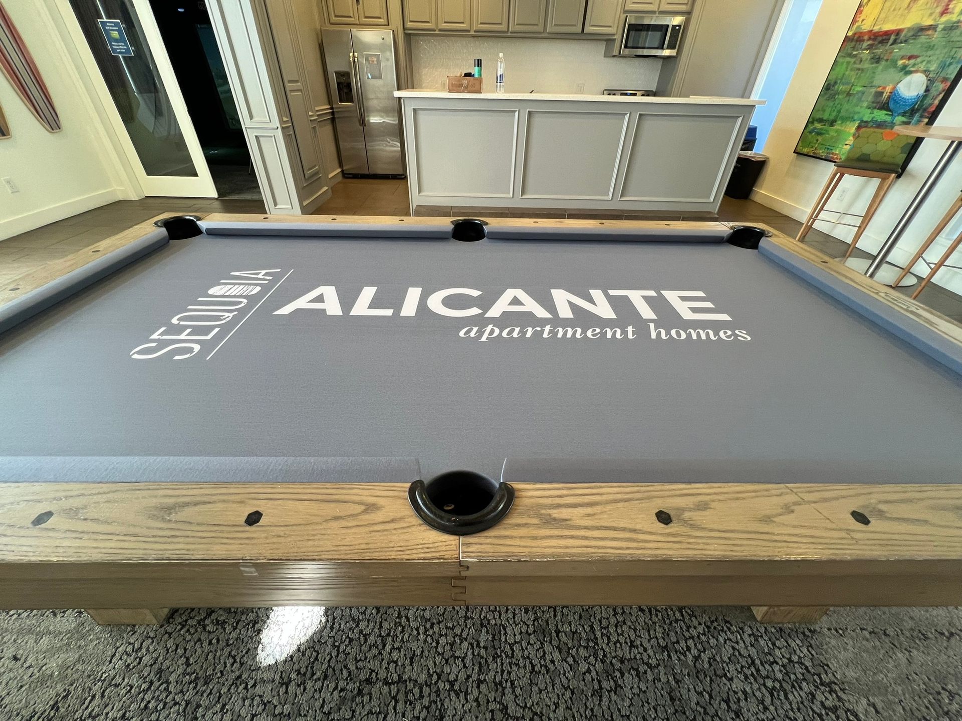 Gray pool table with Alicante Apartment Homes logo in a bright kitchen game room