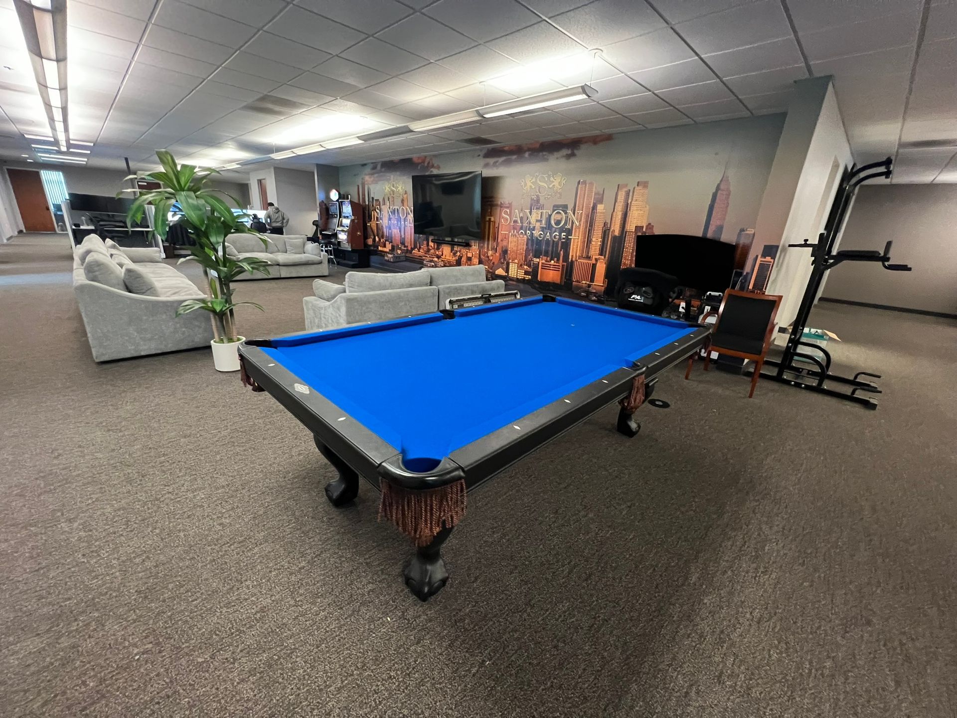 Basement rec room with a blue pool table, couch, TV, and gym equipment under fluorescent lights