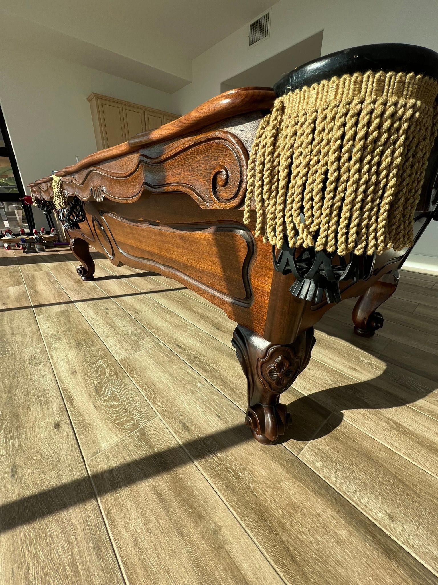 Ornate carved wooden sofa with gold fringe in a sunlit room on a tiled floor