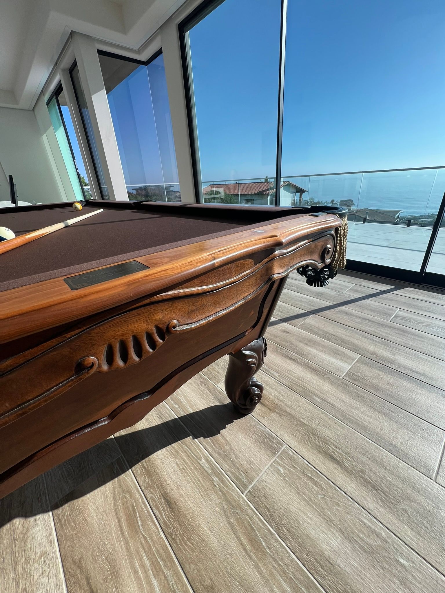 Brown piano in a sunlit room with floor-to-ceiling windows overlooking water and a bridge