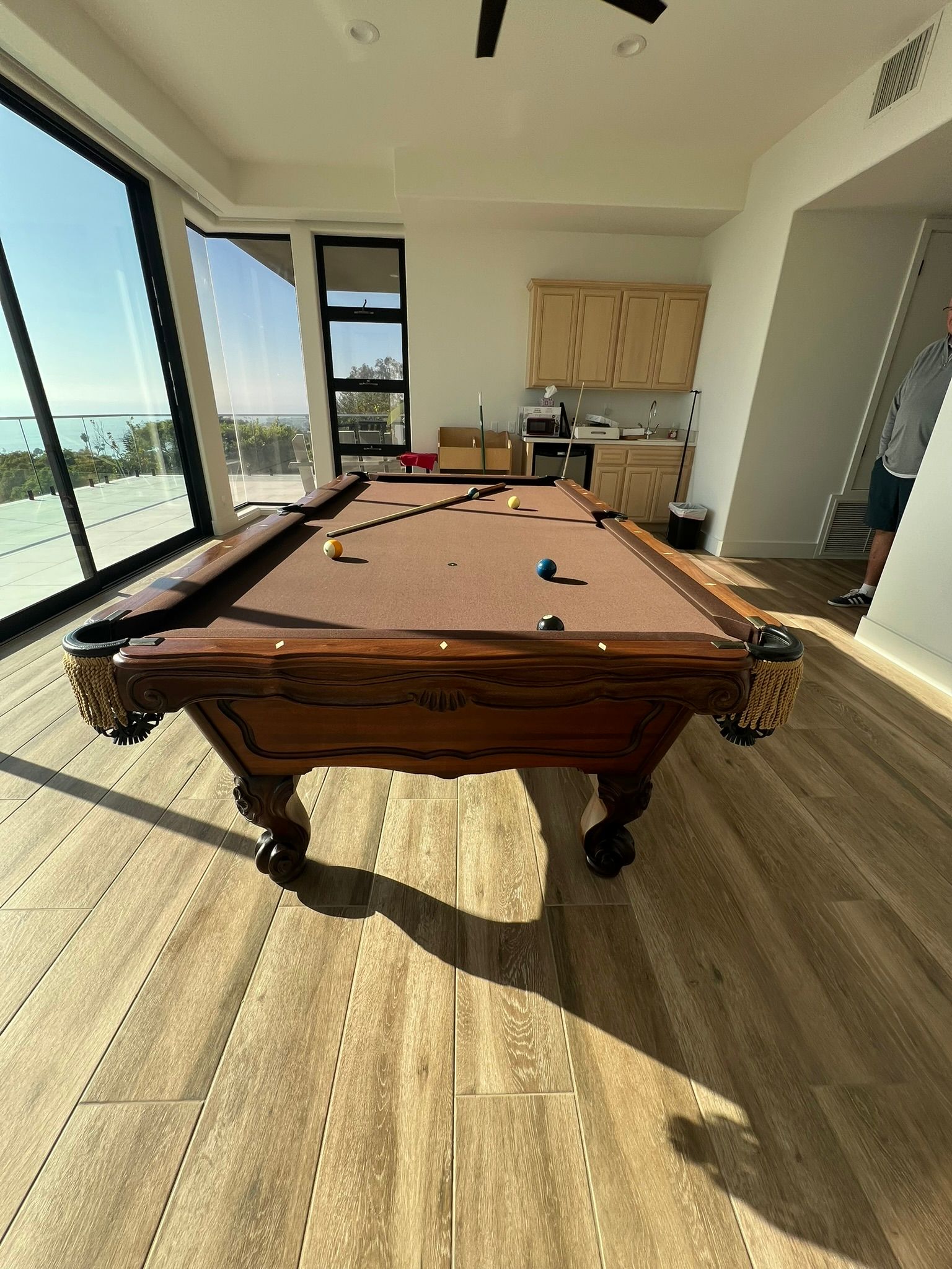 Bright pool table in a sunlit modern room with large windows and wood flooring.