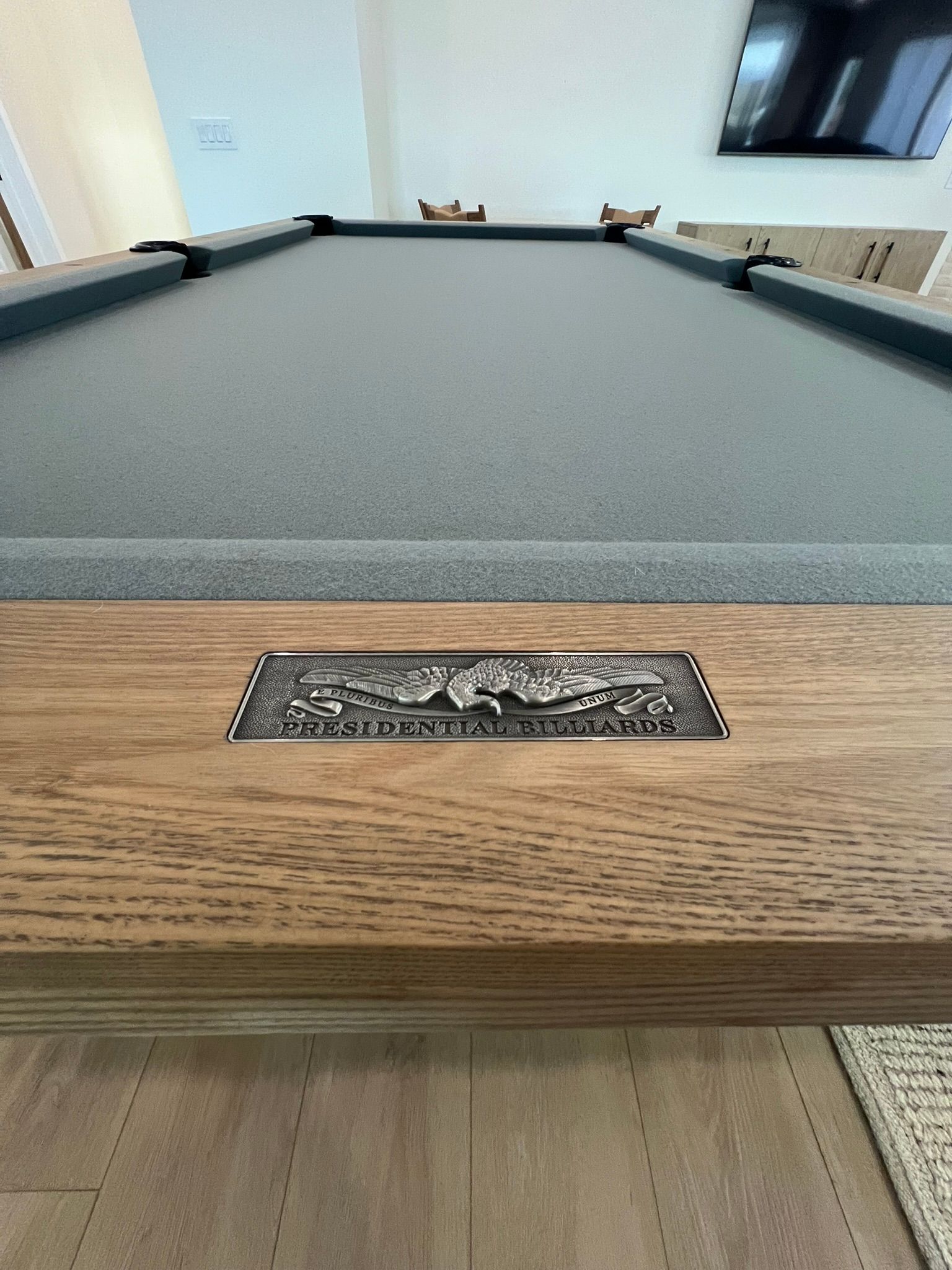 Close-up of a pool table with gray felt and wooden rail in a bright room.