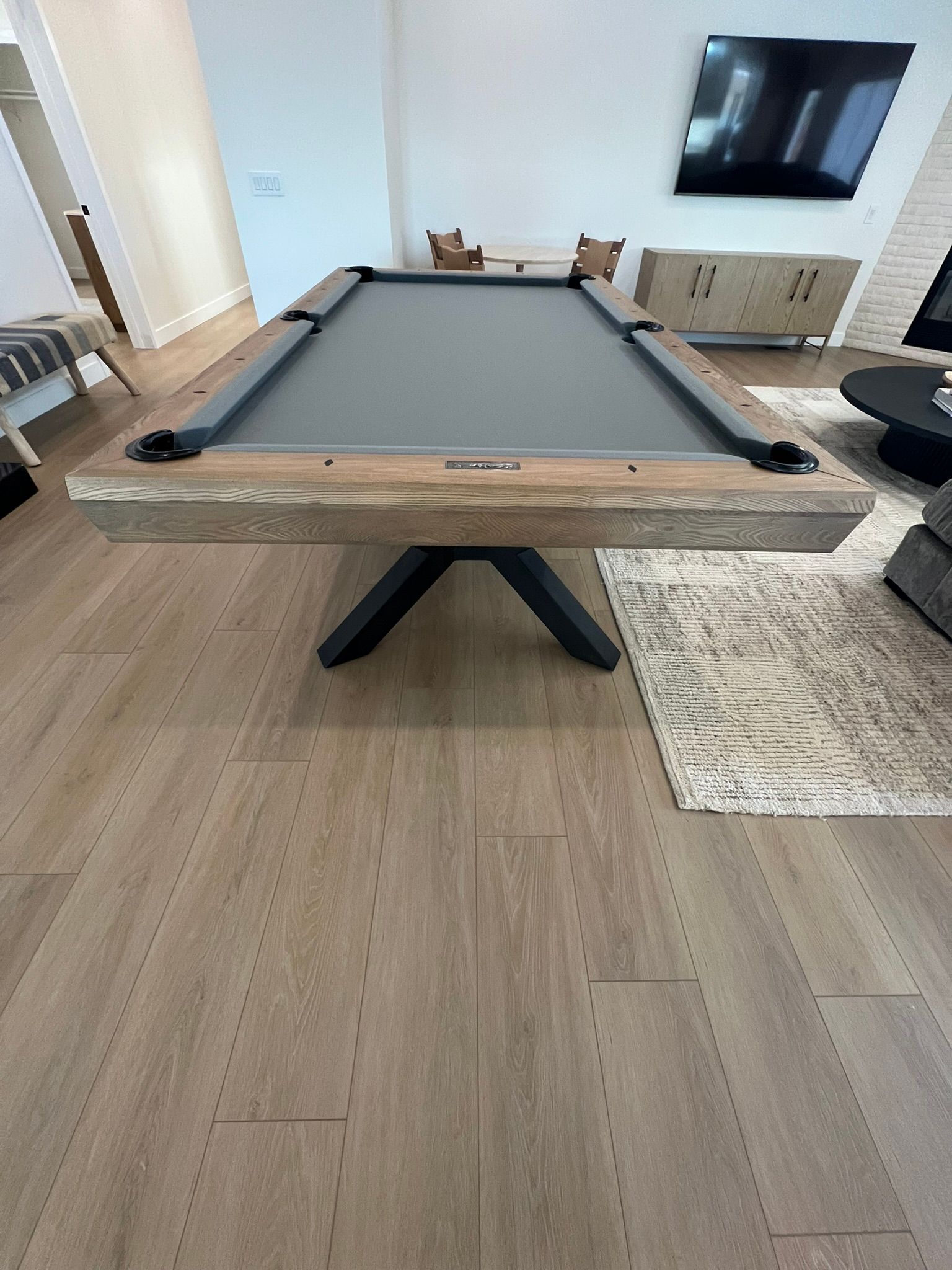 Pool table in a bright living room with hardwood floors and a wall-mounted TV.