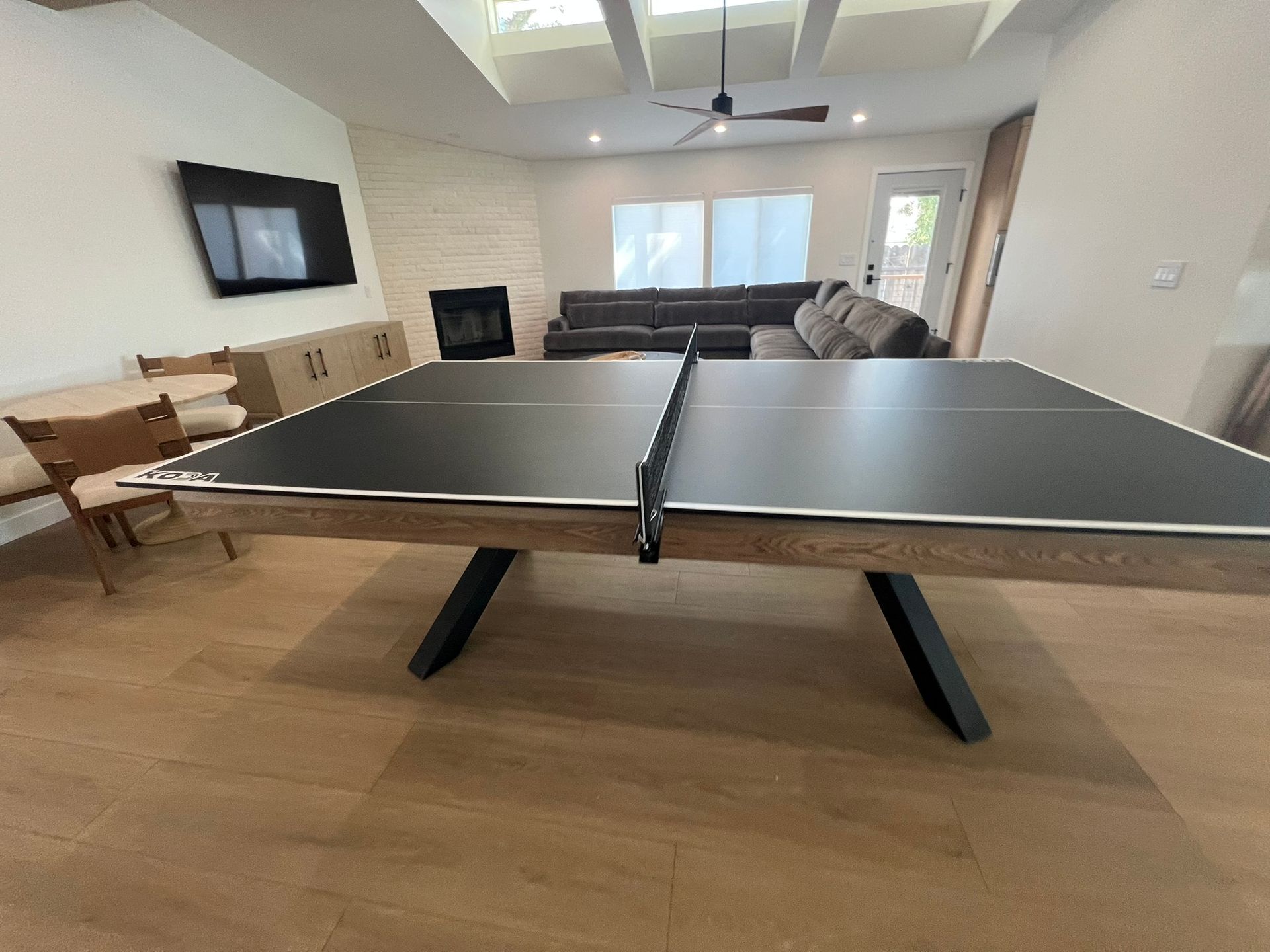 Modern living room with a ping-pong table, wall-mounted TV, and sofa seating
