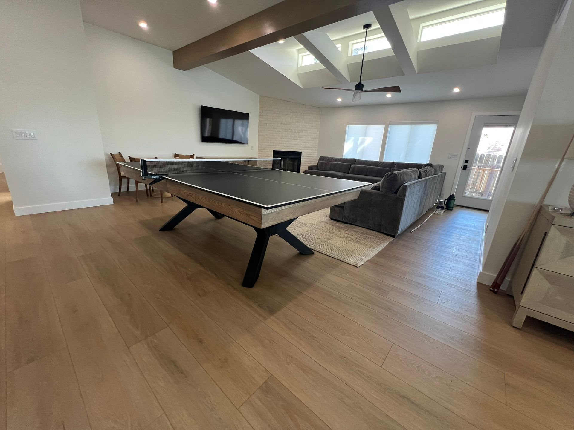 Modern open-plan living room with a pool table, sectional sofa, wall TV, and large windows