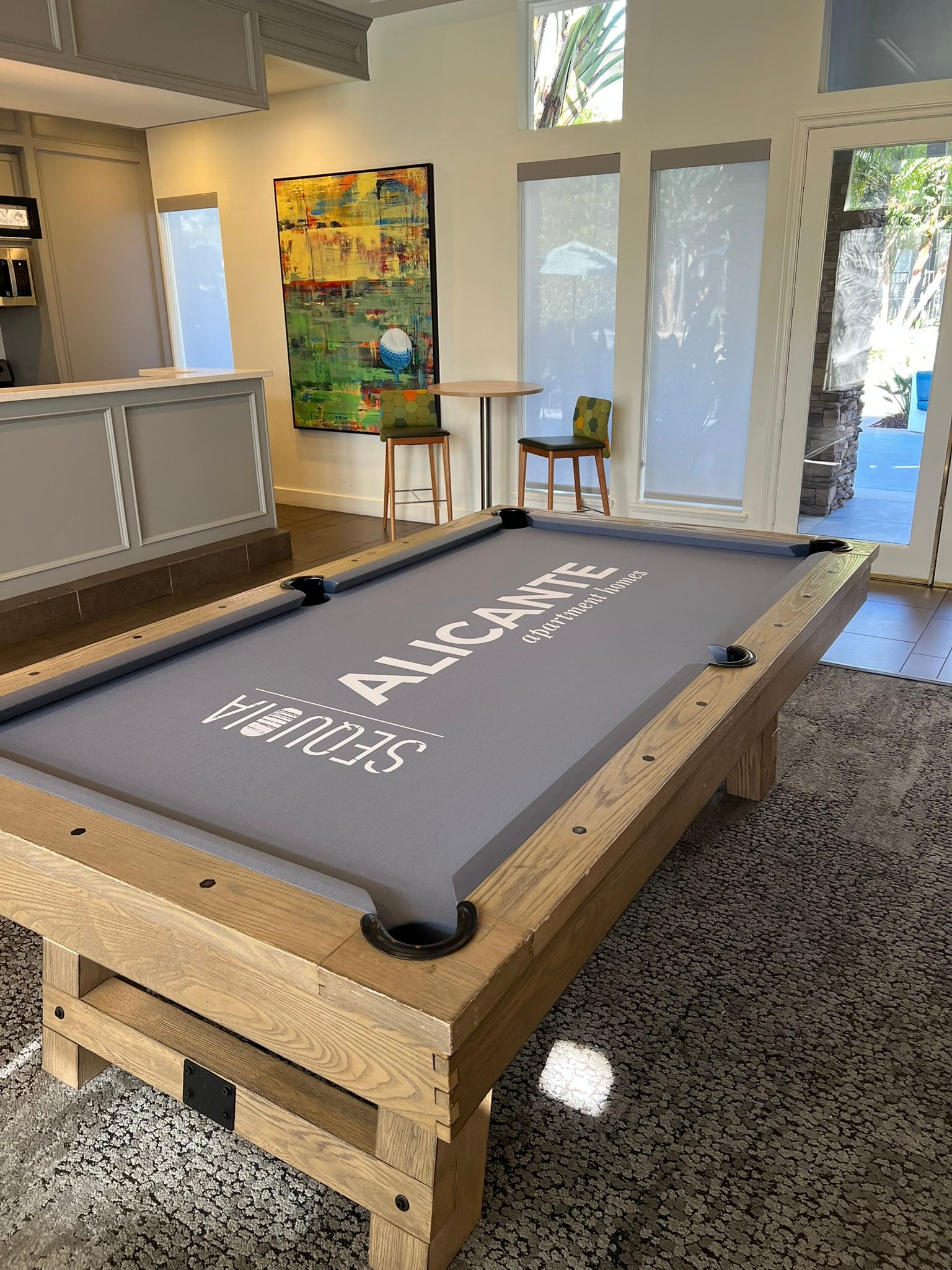 Modern lobby with a gray wooden pool table and large glass doors overlooking greenery