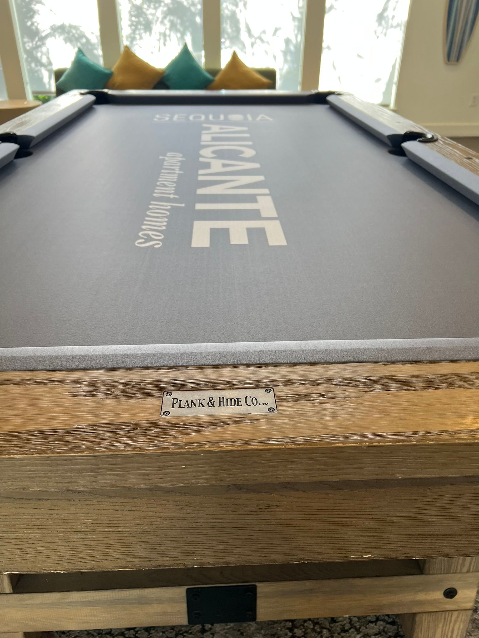 Pool table with gray felt and triangle of balls at the far end in a bright room