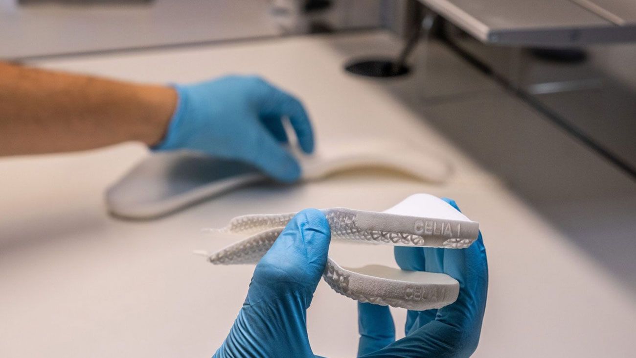 A person wearing blue gloves is holding a 3D-printed custom orthotics