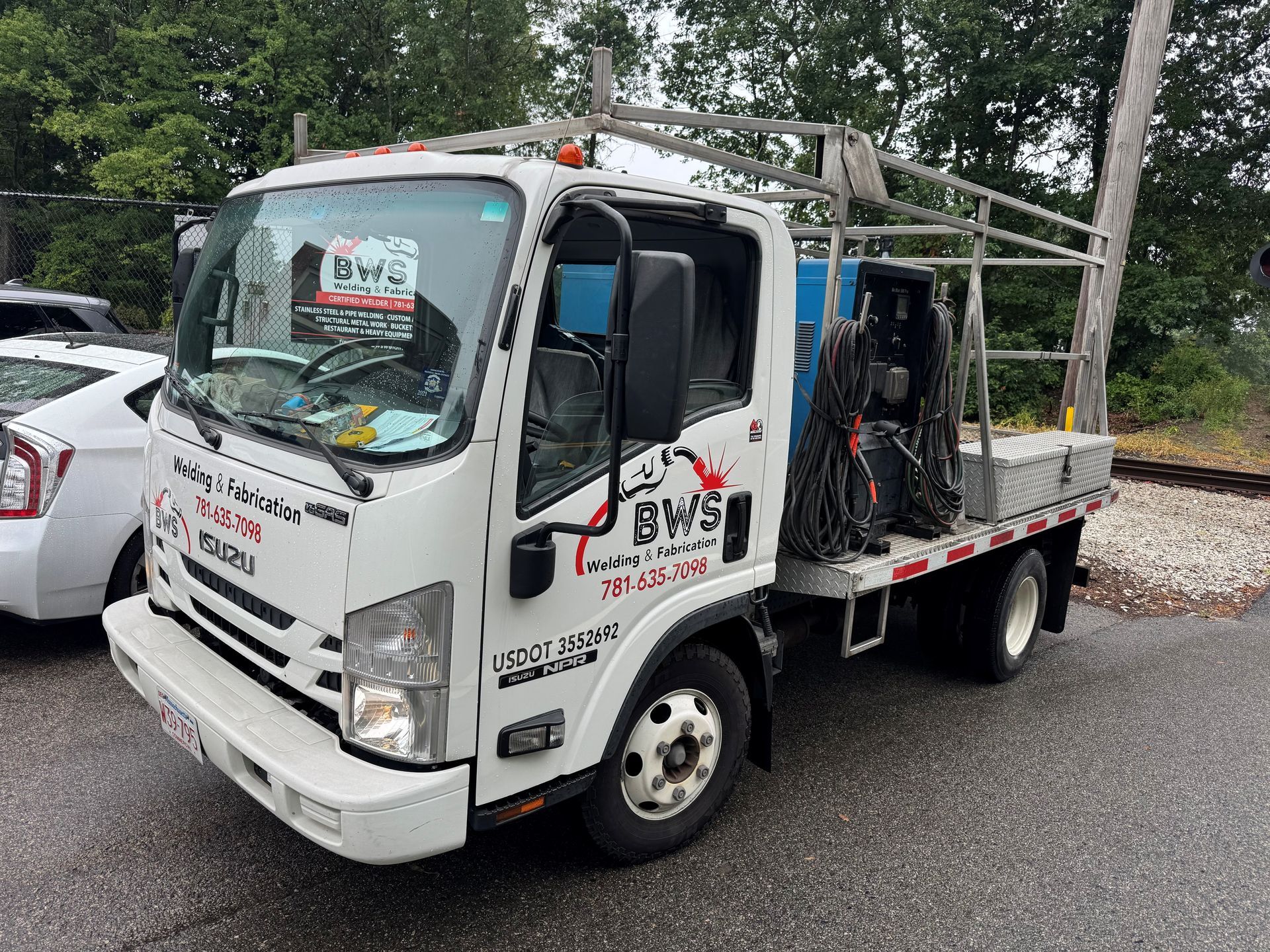 White flatbed tow truck parked on a road, with trees and cars in the background.