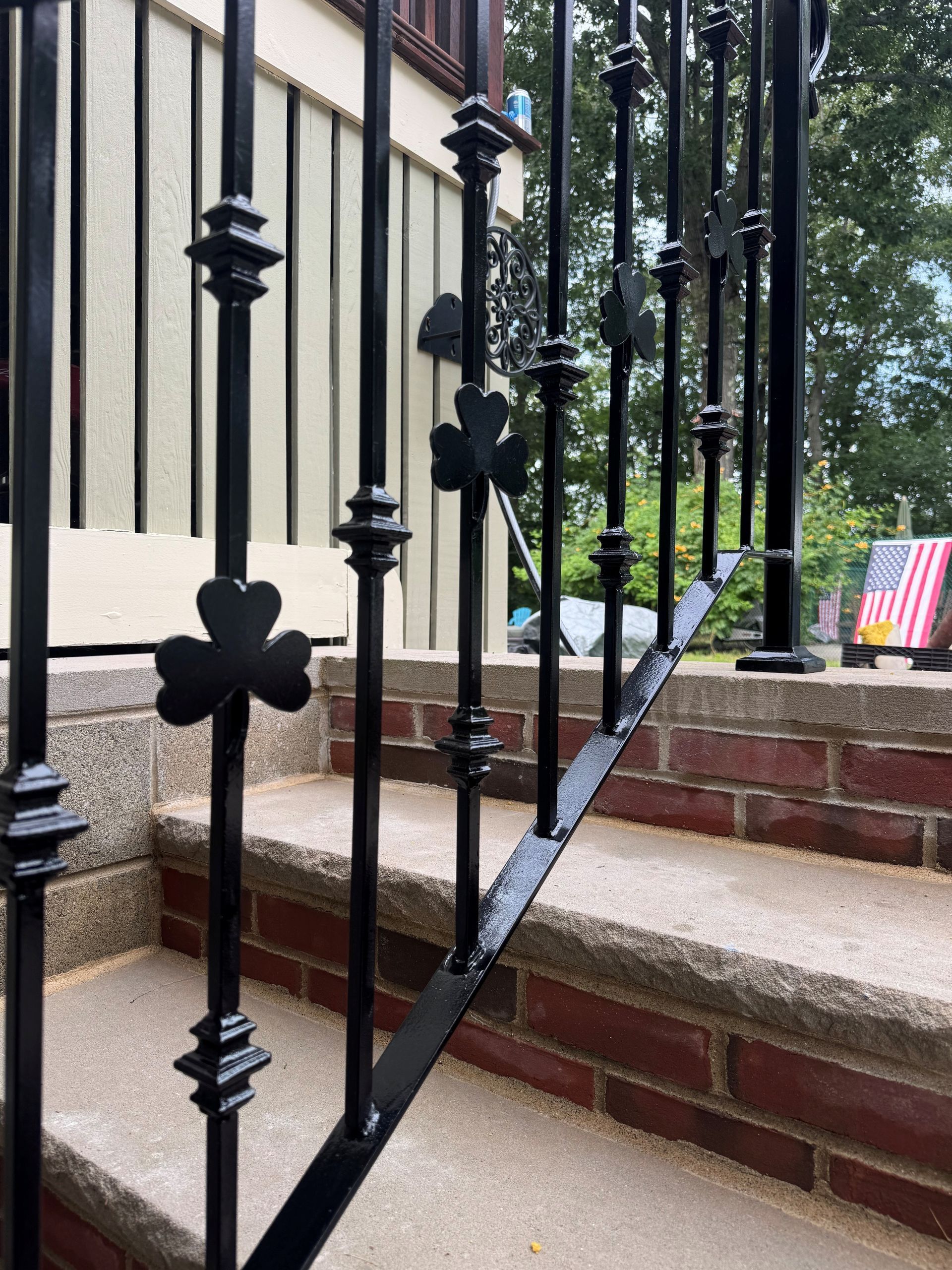 Black iron railing with clover details beside brick steps and a house porch
