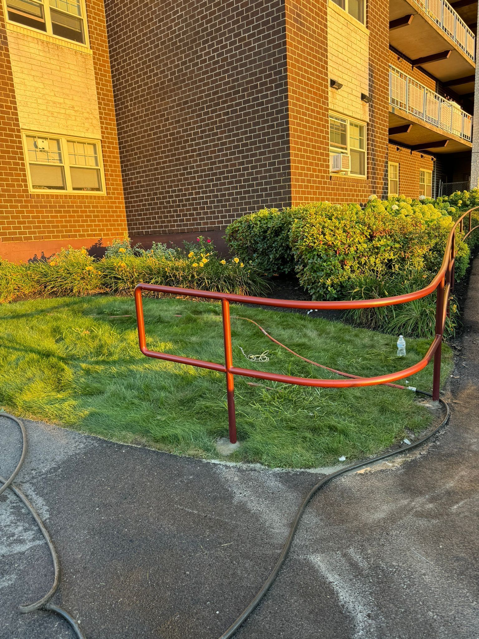 Red metal handrail beside a grassy slope and brick apartment building entrance.