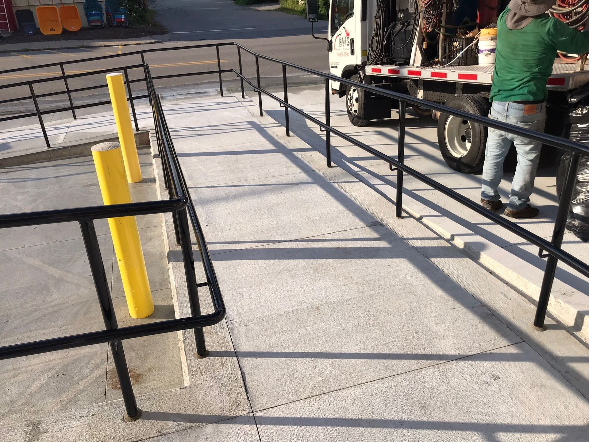 Concrete ramp with black handrails and yellow bollards beside a truck at a loading dock