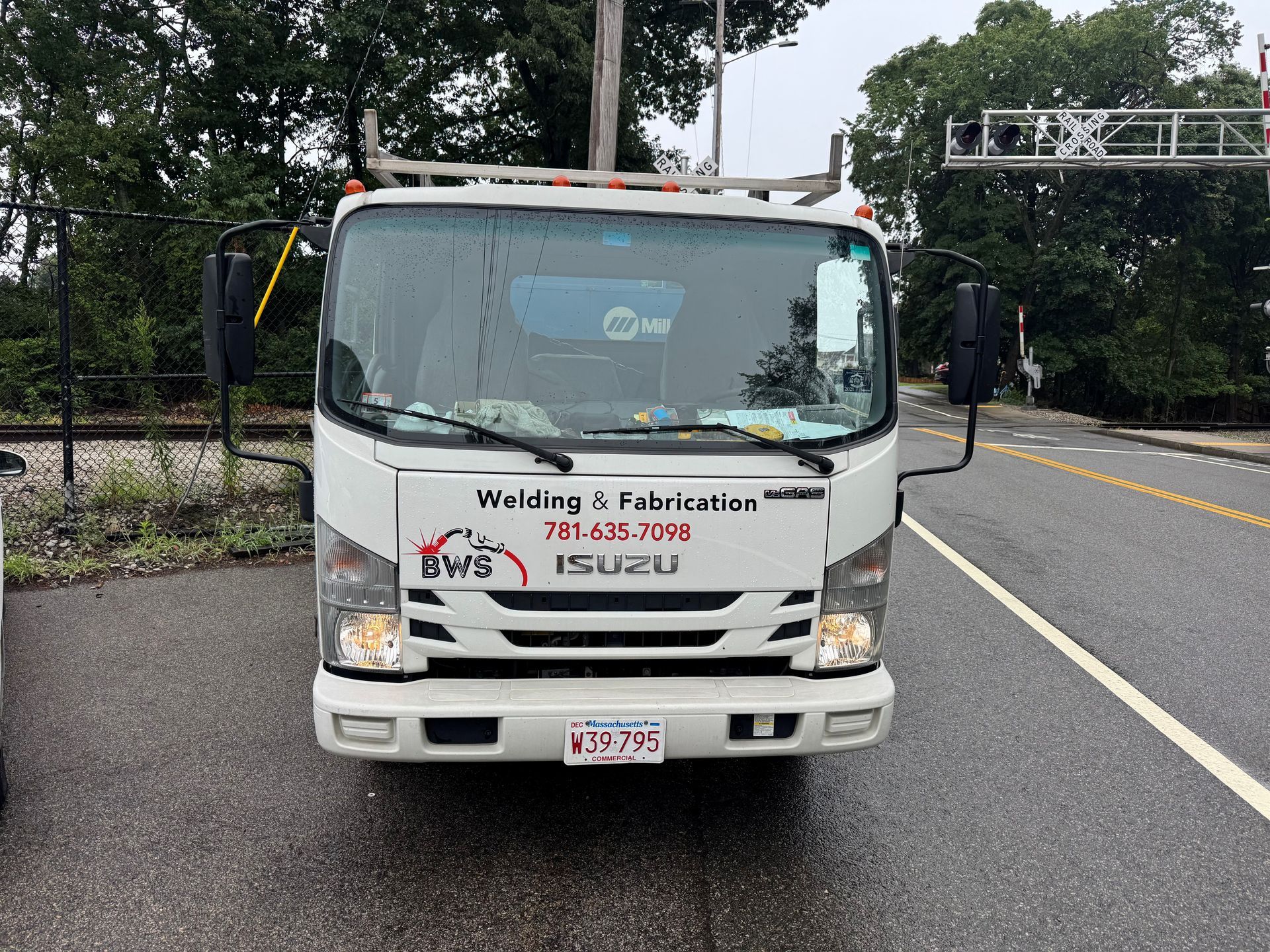 White Isuzu box truck parked on a wet roadside, with company signage on the front.