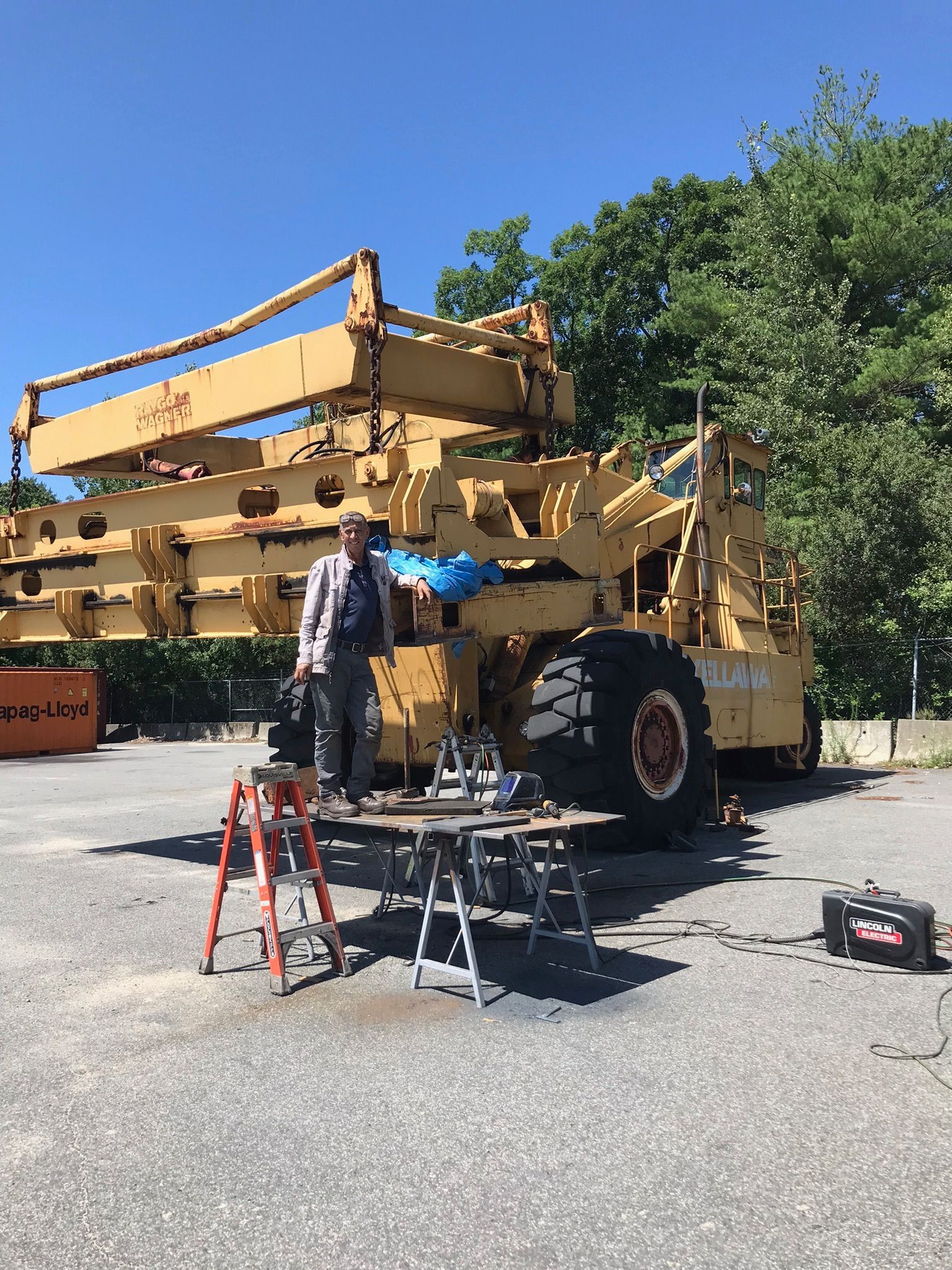 Person standing beside large yellow utility machine with tools on the ground in a parking lot