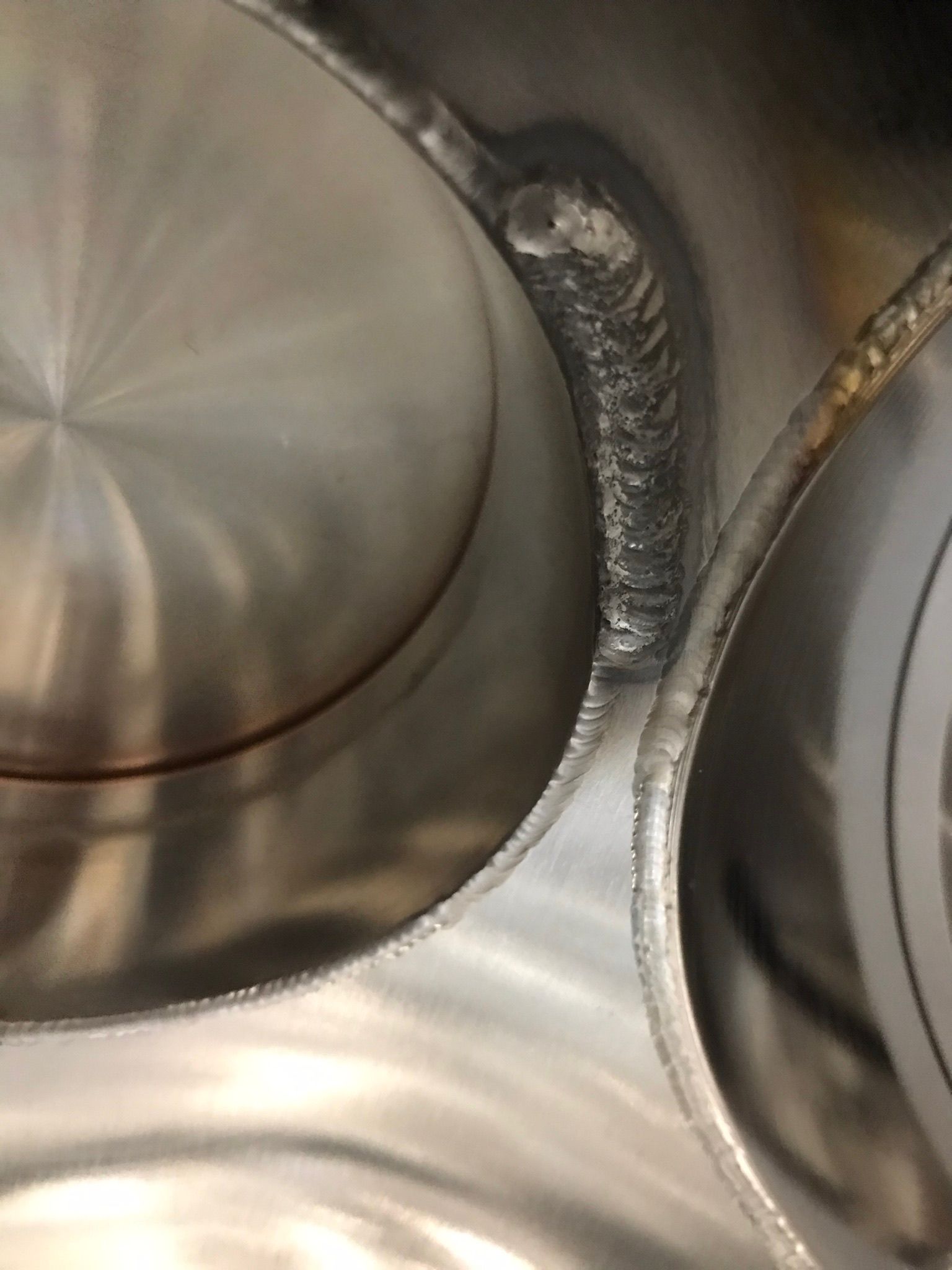 Two metal pot lids in a stainless steel sink, with a dark grime line between them.