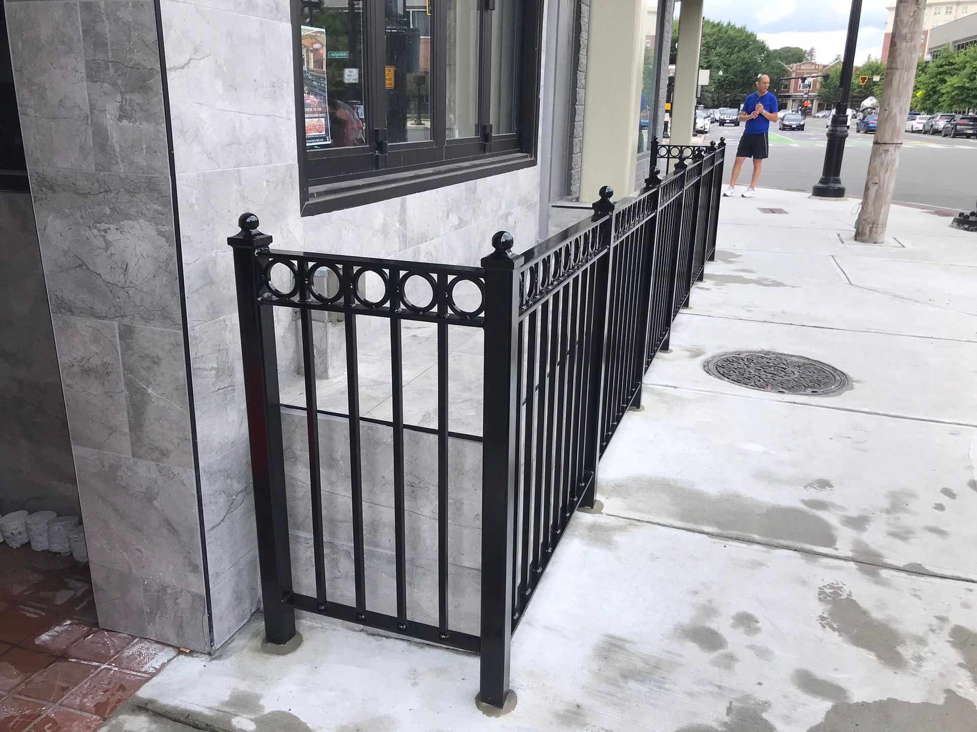 Black wrought-iron railing around a recessed storefront entrance on a city sidewalk, with one pedestrian in the distance