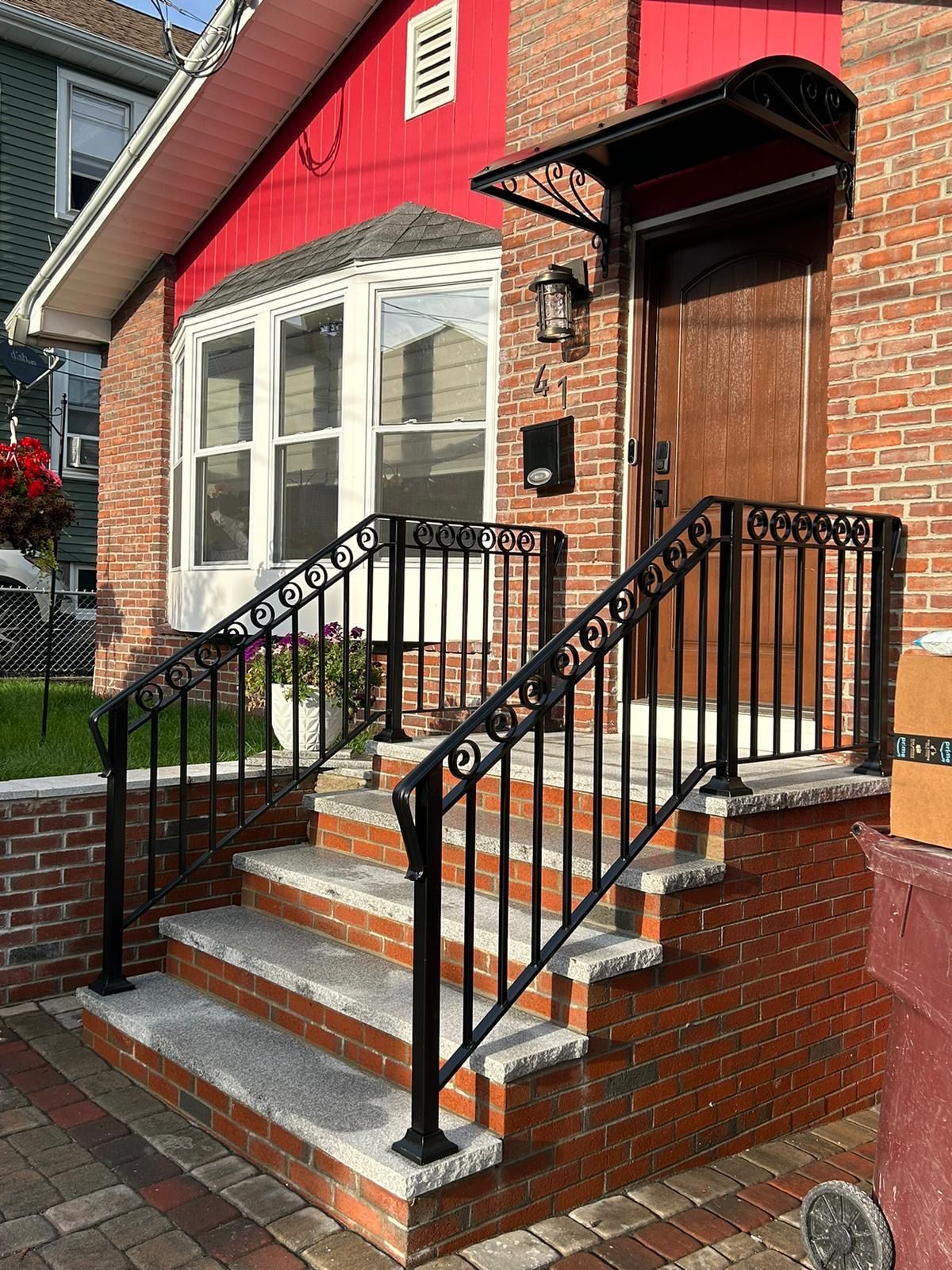 Brick house entrance with steps, black railings, and red siding on a small front stoop.