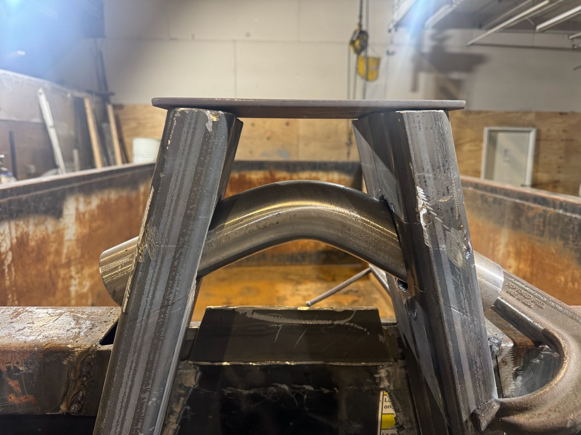 Metal fabrication setup with a curved pipe section and black supports inside a rusted industrial container