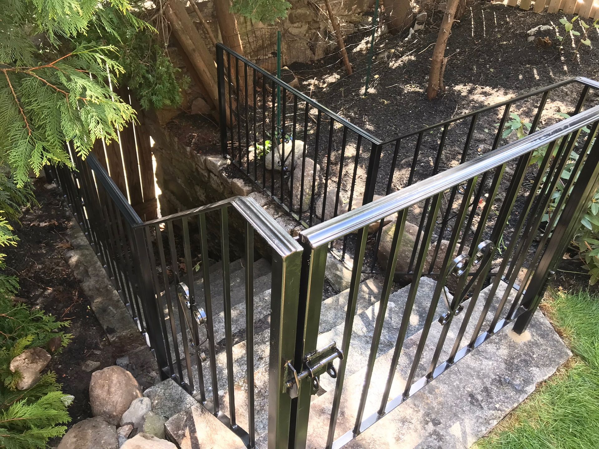 Black metal gated stairway beside a stone path and greenery