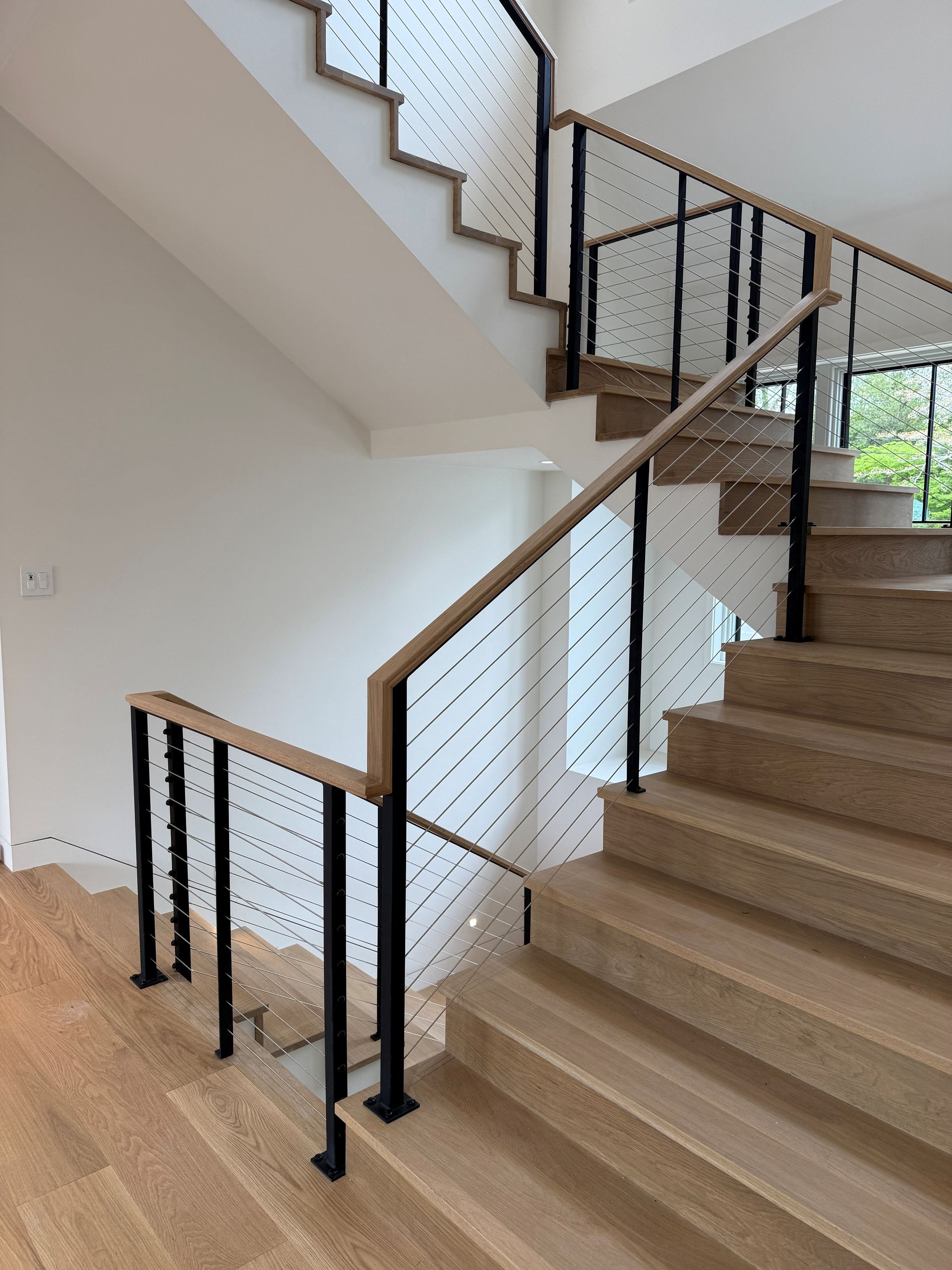 Indoor staircase with tan carpet, black metal railing, and a white wall near a bright window.