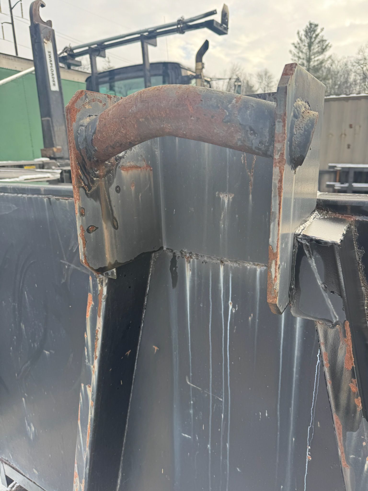 Rusty bent pipe atop a dark industrial tank or vessel outdoors