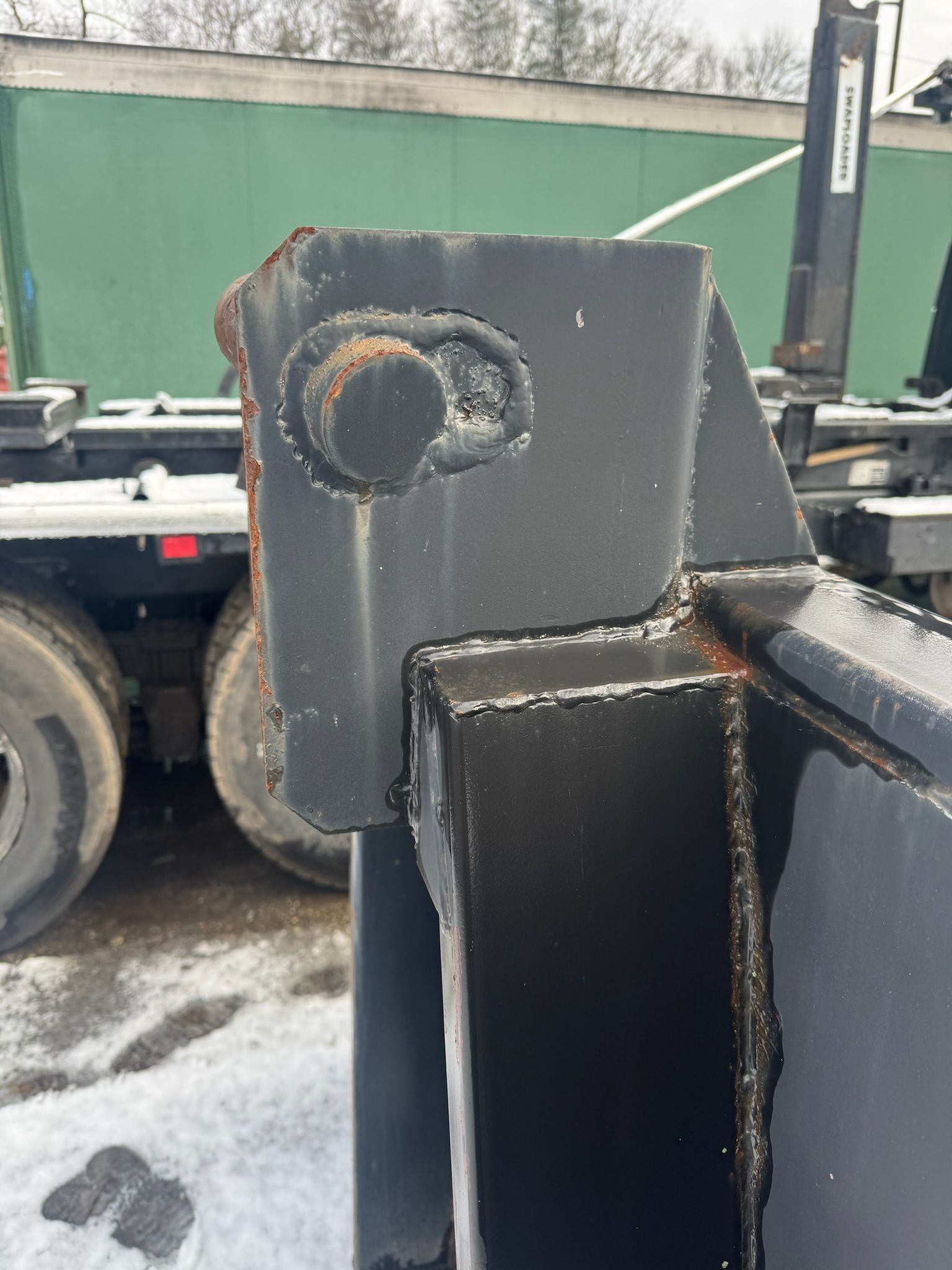 Close-up of a black metal hitch joint with rust, on a trailer in a snowy industrial yard