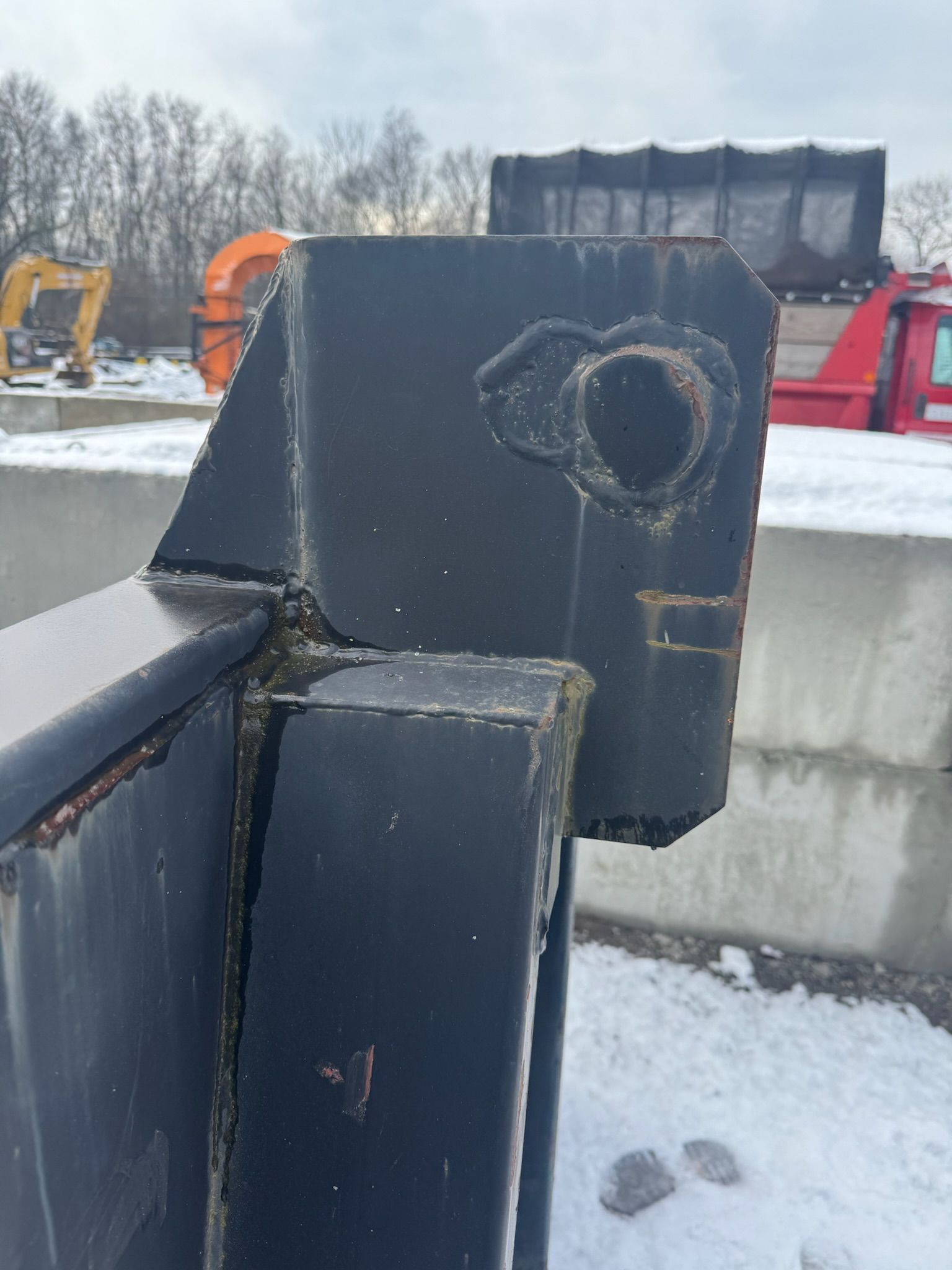 Close-up of a black metal railing bracket with a snow-covered industrial yard in the background.
