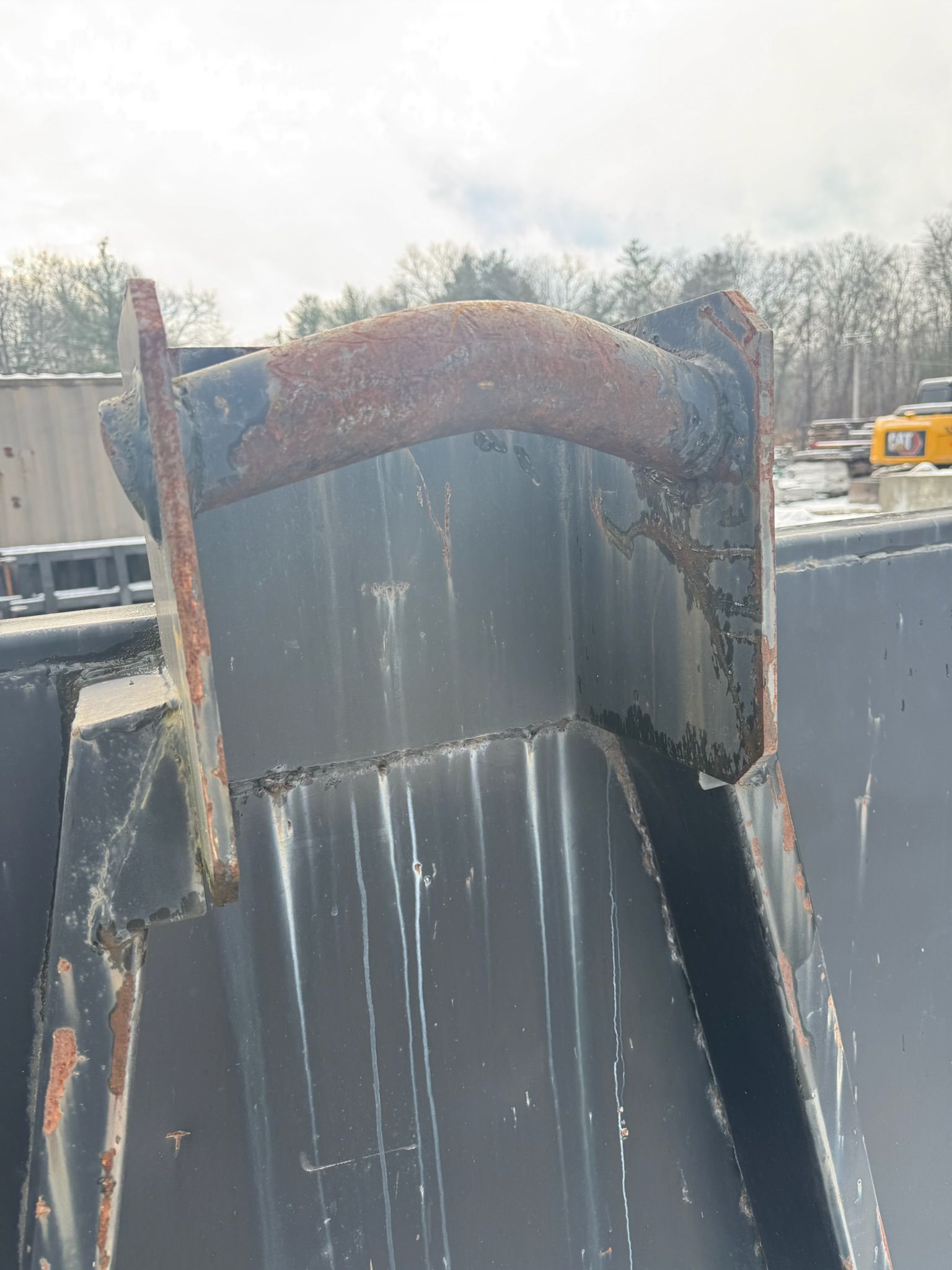 Rusty industrial metal chute in a snowy outdoor yard, with a worker and machinery in the background
