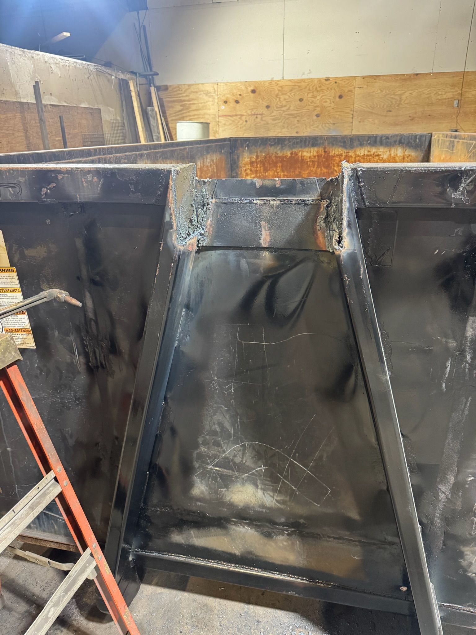 Black metal machinery parts in a workshop, with a large triangular panel and orange rust along the top edge