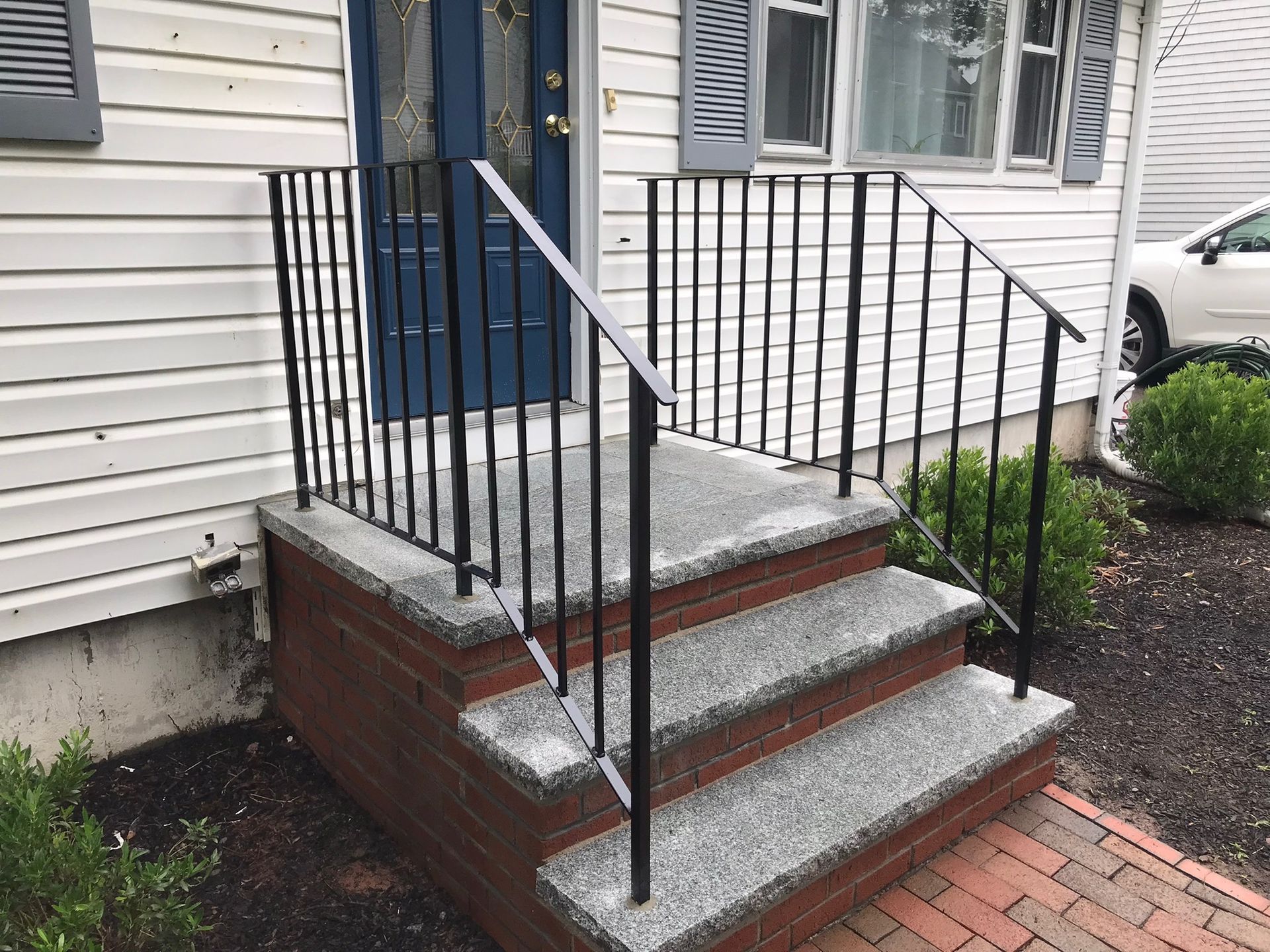 Front steps to a house with black railings, white siding, and a blue door.