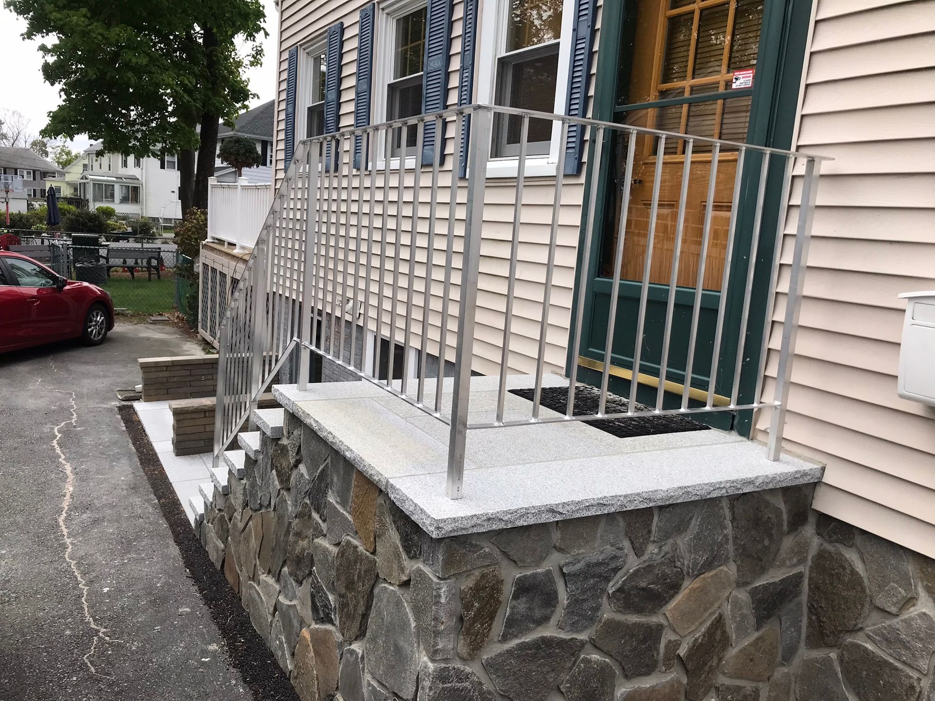 Stone-front porch with metal railings and steps beside a house on a residential street