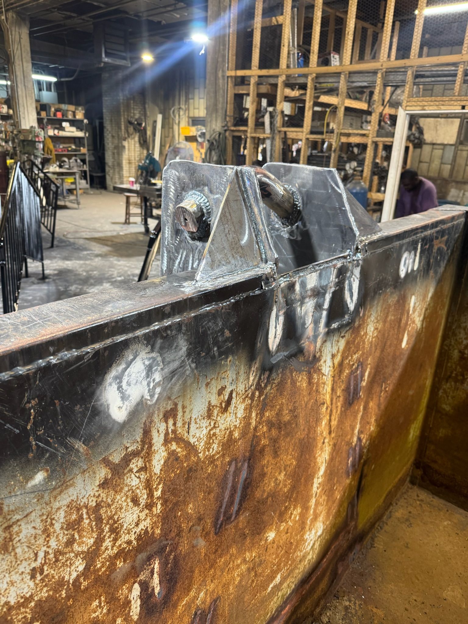 Rusty industrial metal tank in a workshop with scaffolding and a person in the background