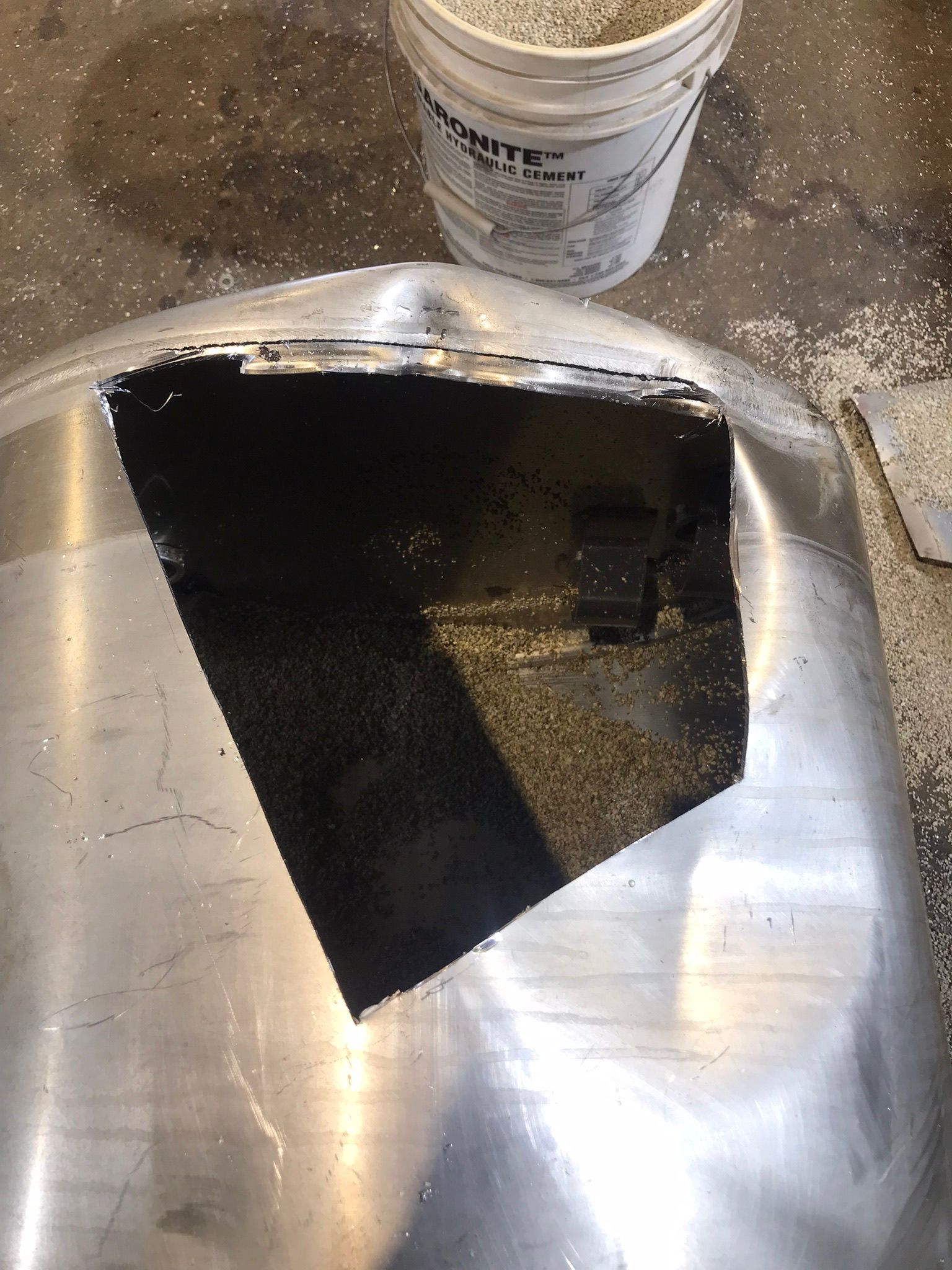 Black paint spilled on a stainless steel sink or counter beside a white paint bucket.