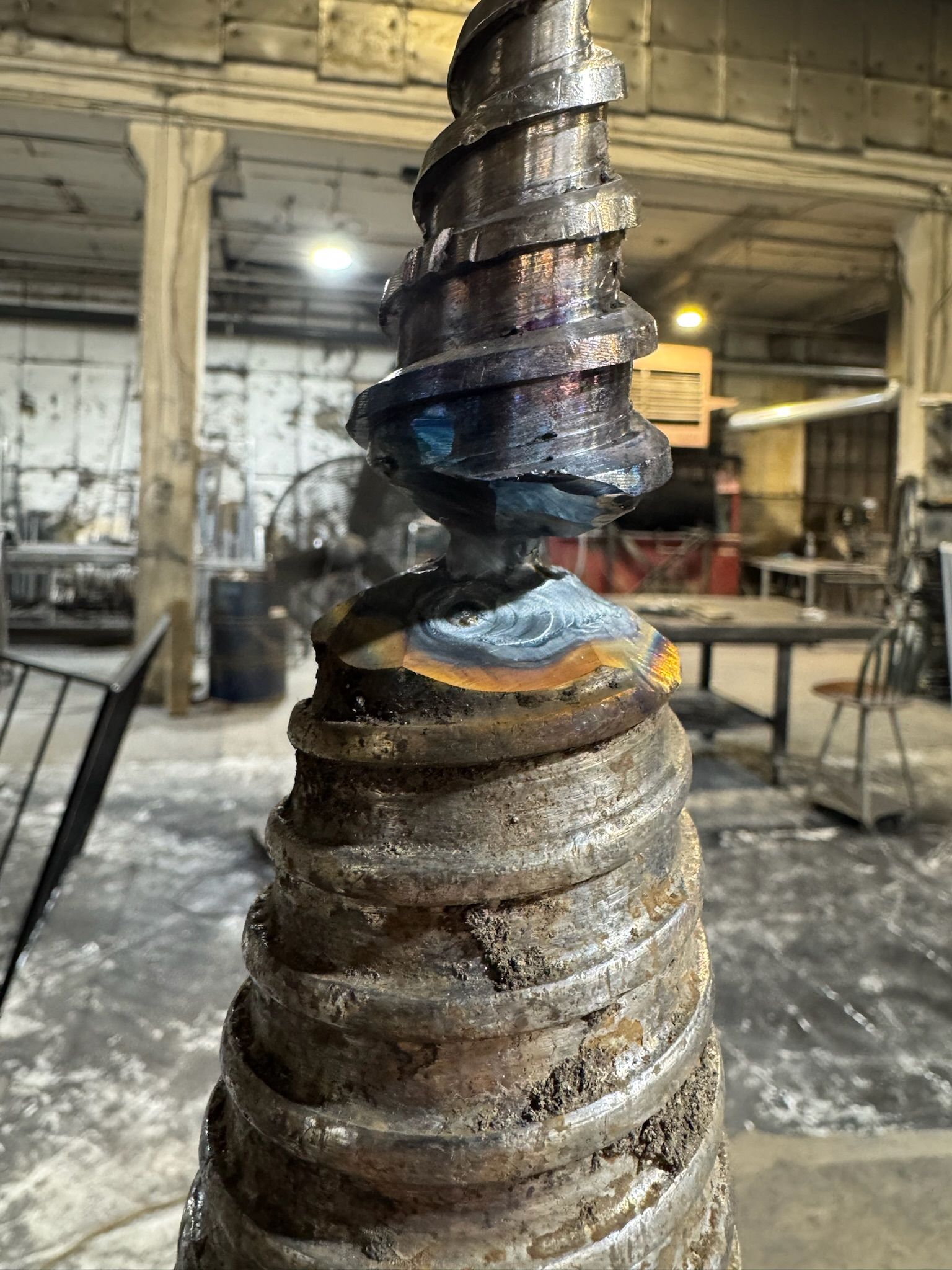 Abstract stacked metal sculpture in an industrial workshop, with twisted silver and bronze rings.