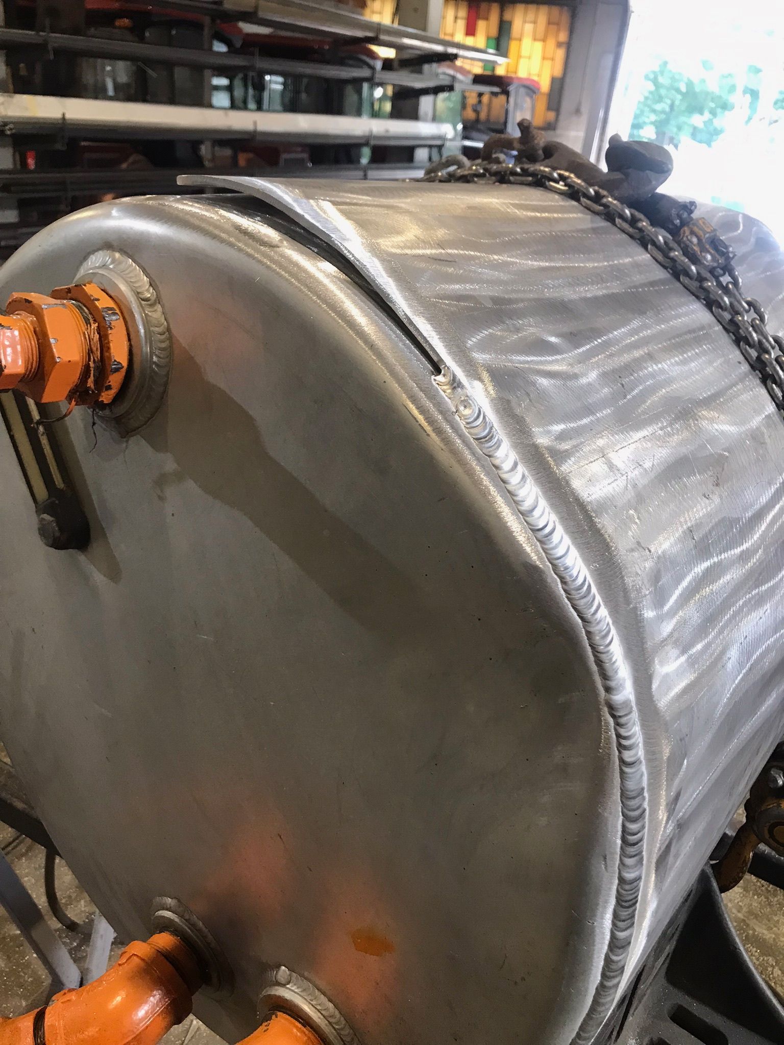 Large metal industrial tank with orange pipe fittings in a workshop setting