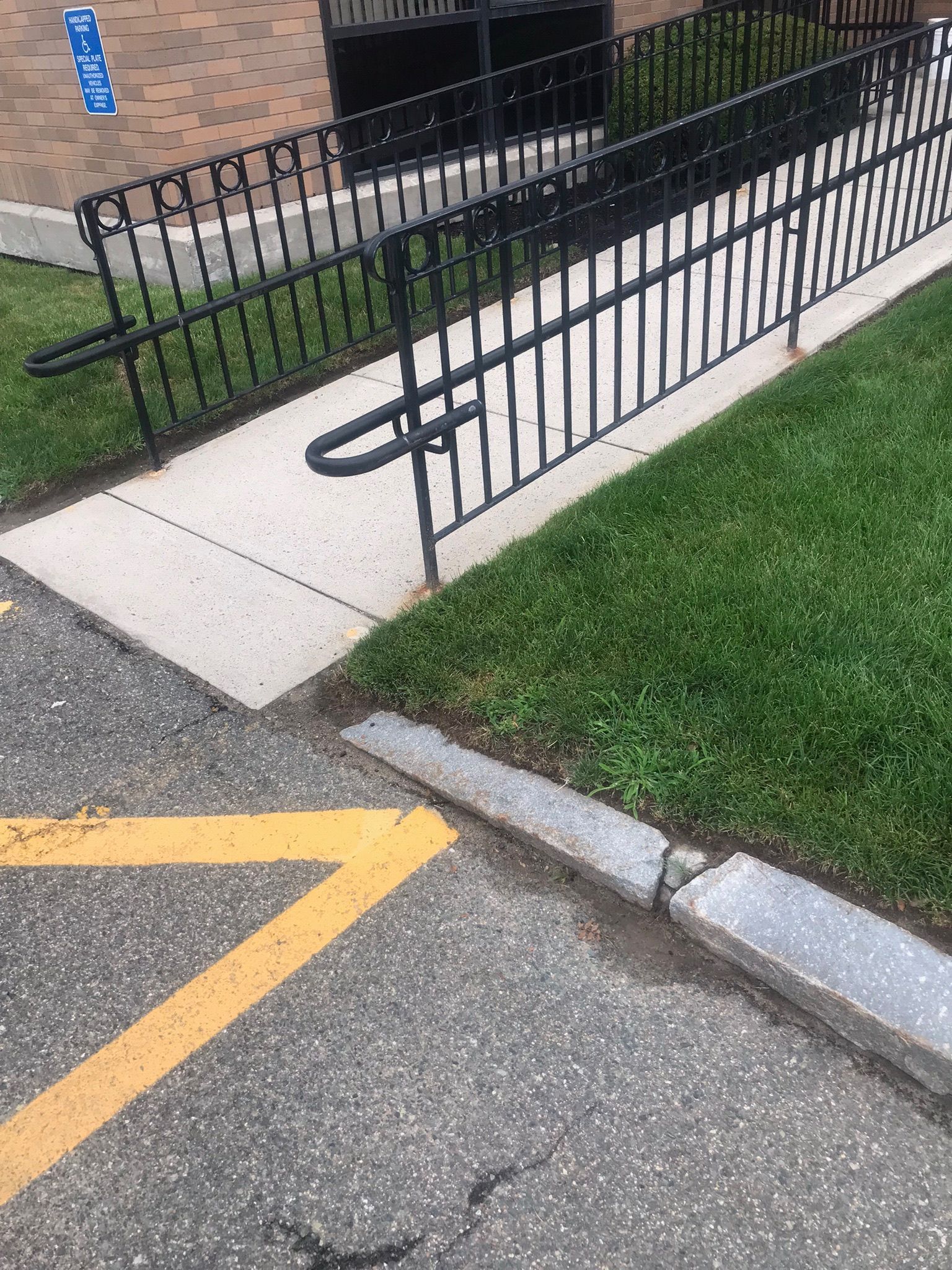 Sidewalk ramp beside a black metal fence, with curb and yellow parking lines on the asphalt.