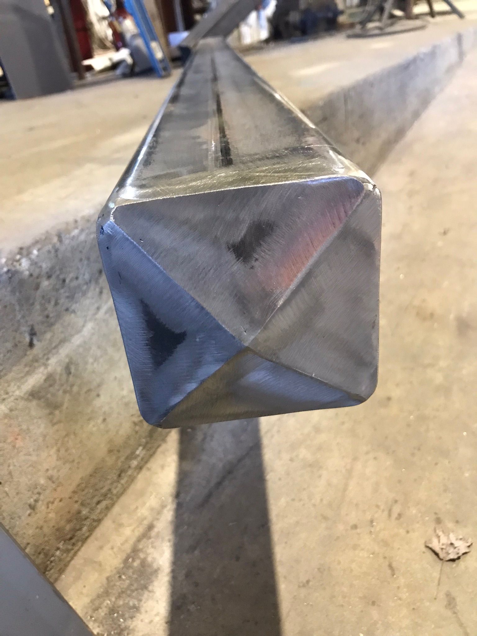 Close-up of a metal square tube end resting on a concrete floor in a workshop.