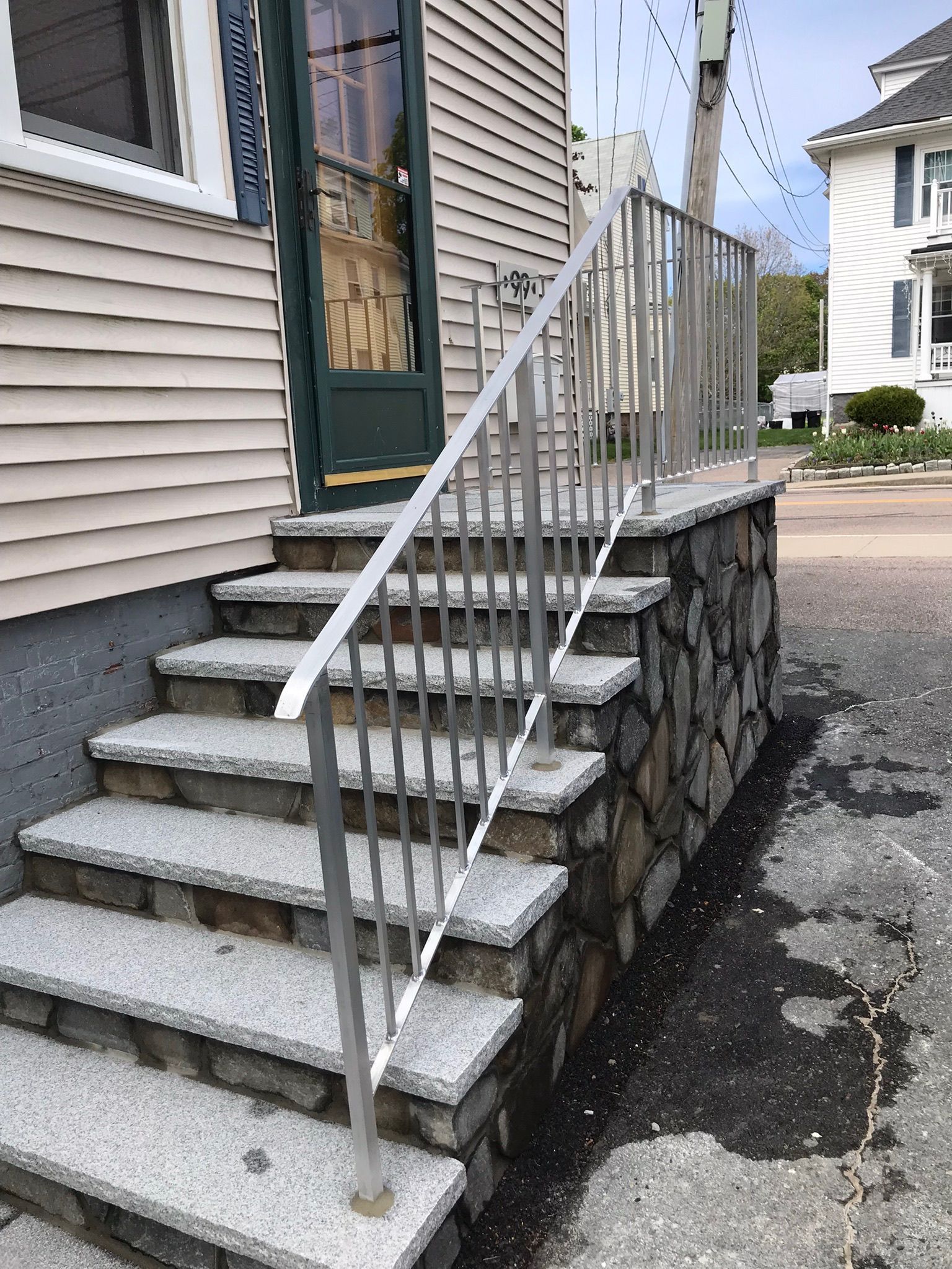 Front steps with white railing leading to a green door beside a stone foundation