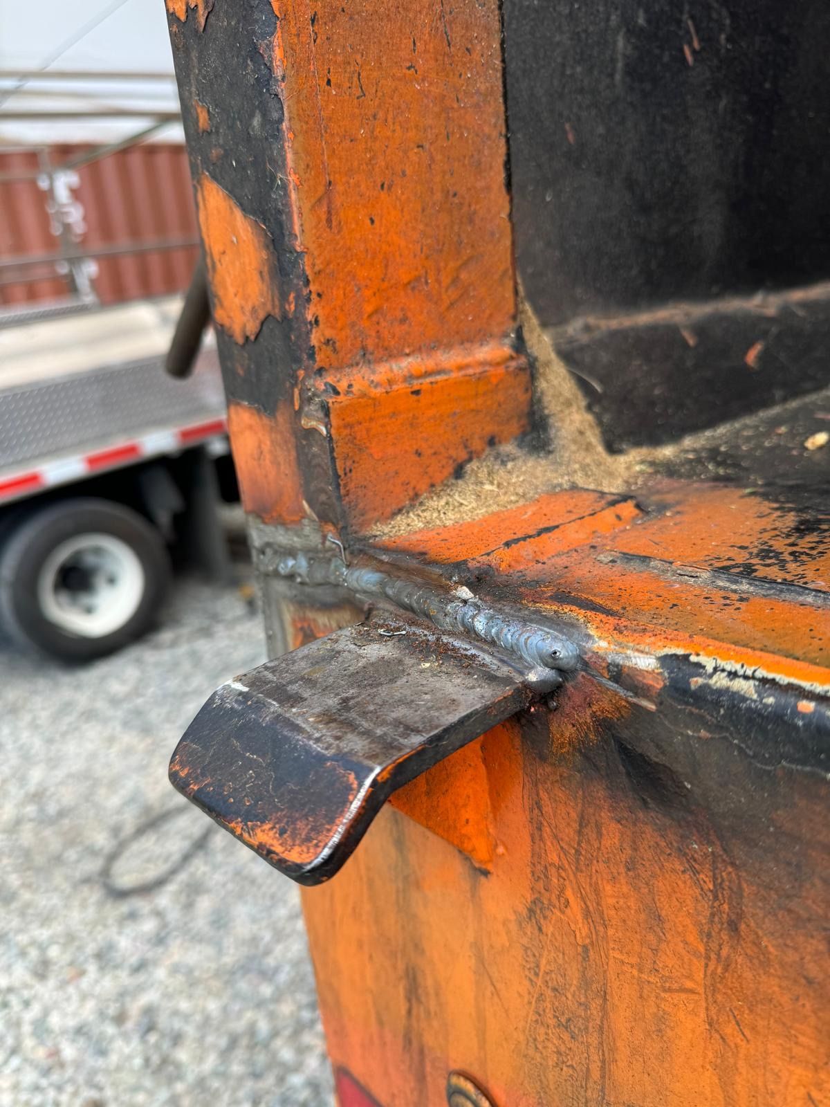 Close-up of a rusty metal latch welded to an orange trailer frame