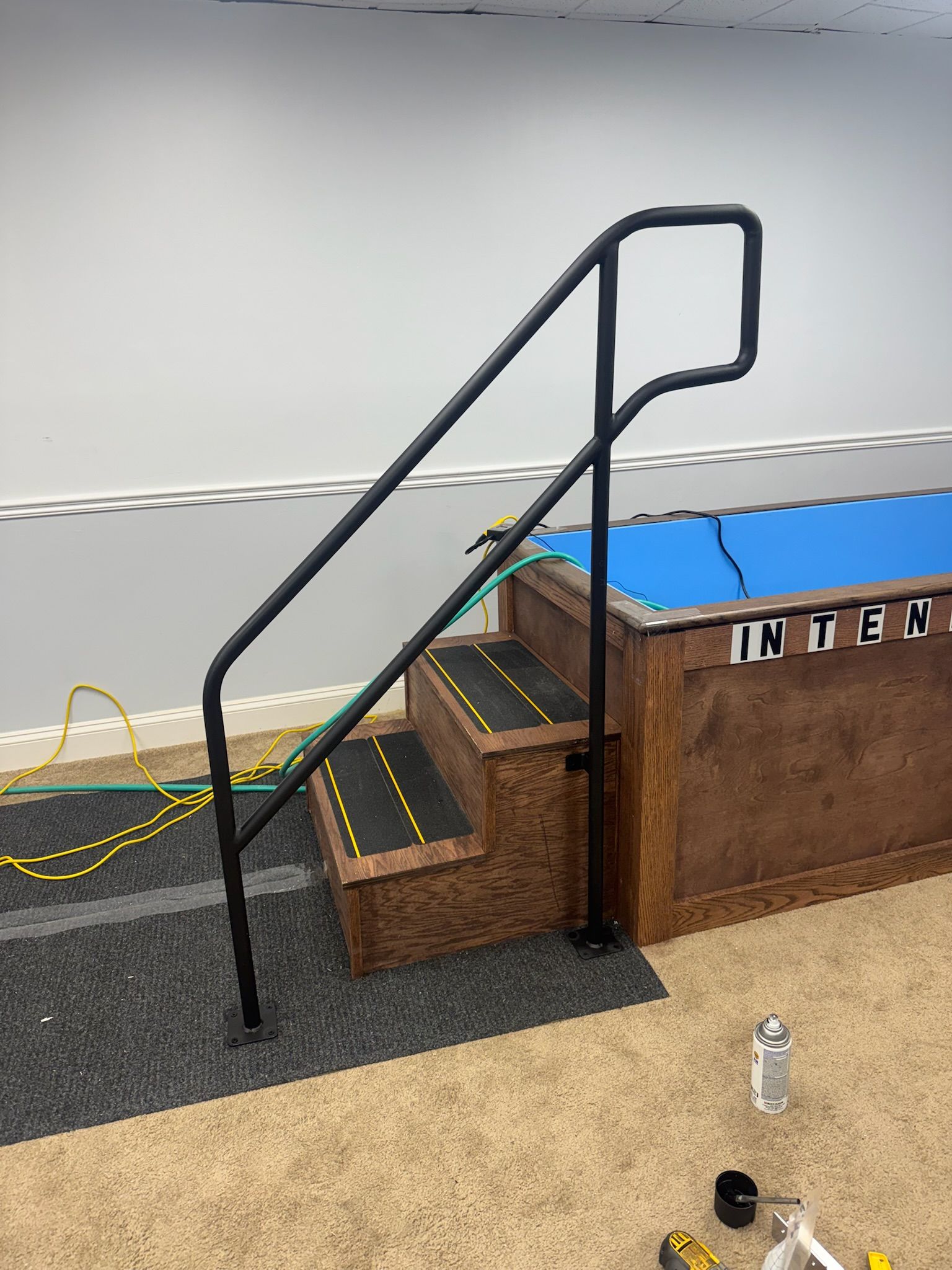 Indoor pool access stairs with black handrails and a small platform beside blue water