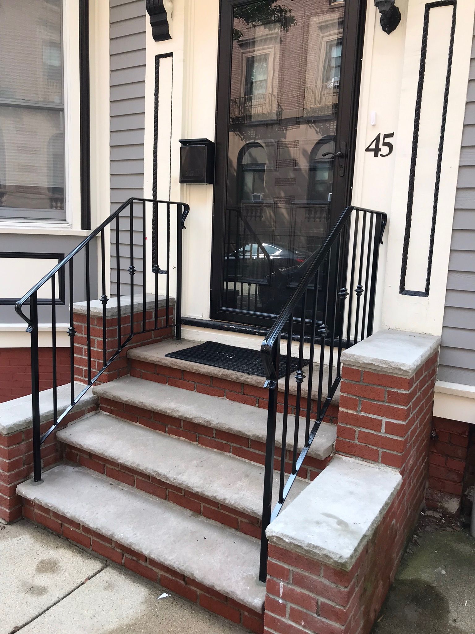 Front steps with black railings leading to a dark door marked 45 on a brick townhouse.