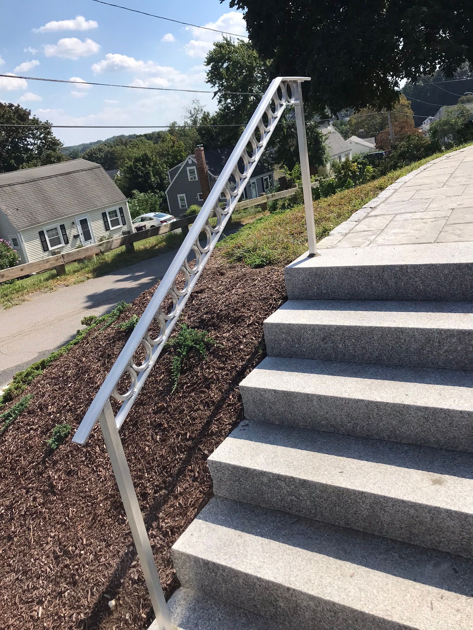Concrete steps with a metal handrail beside a sloped walkway under a blue sky.