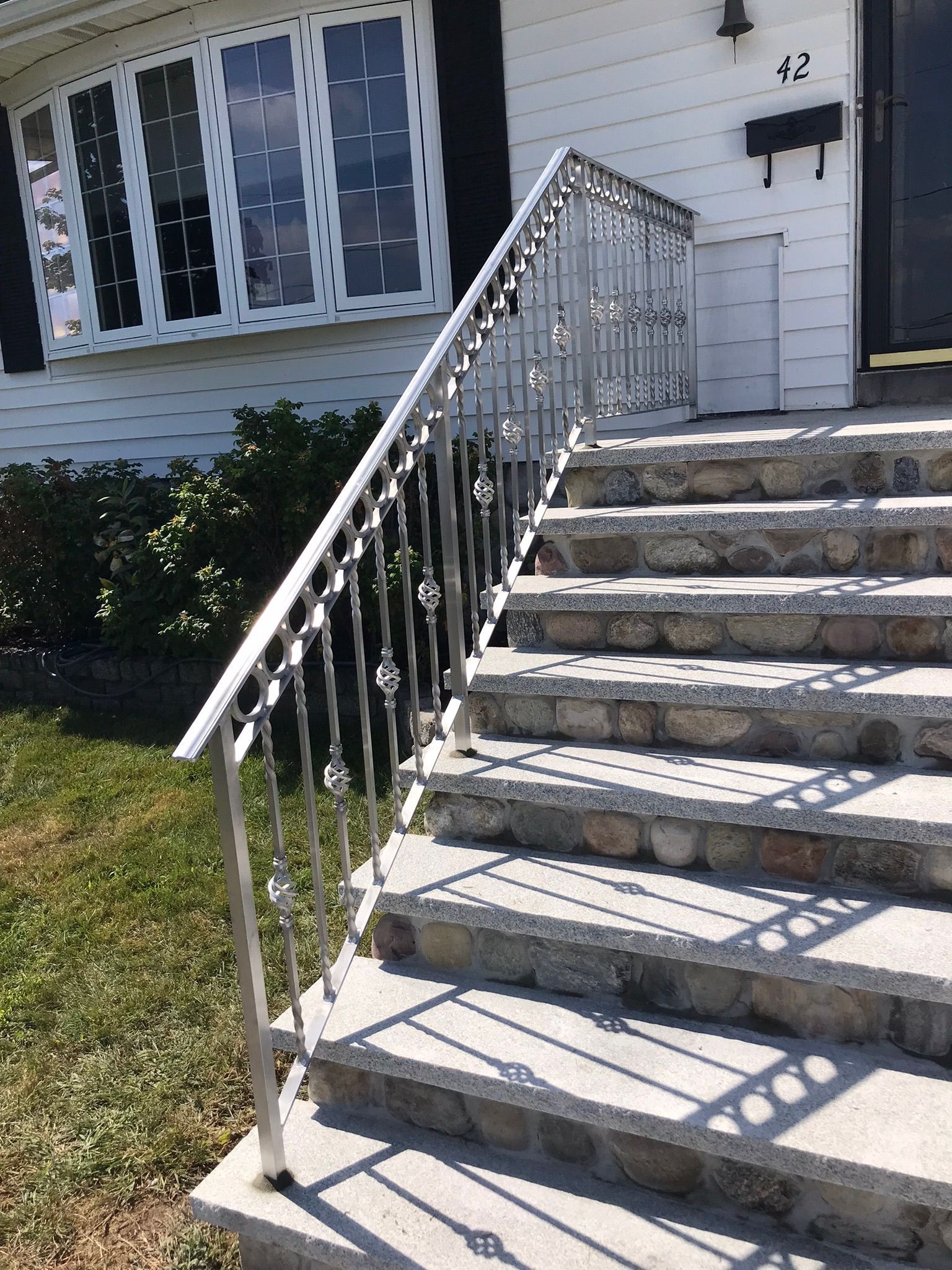 Front steps to a white house with a metal railing and black mailbox, seen in bright sunlight.