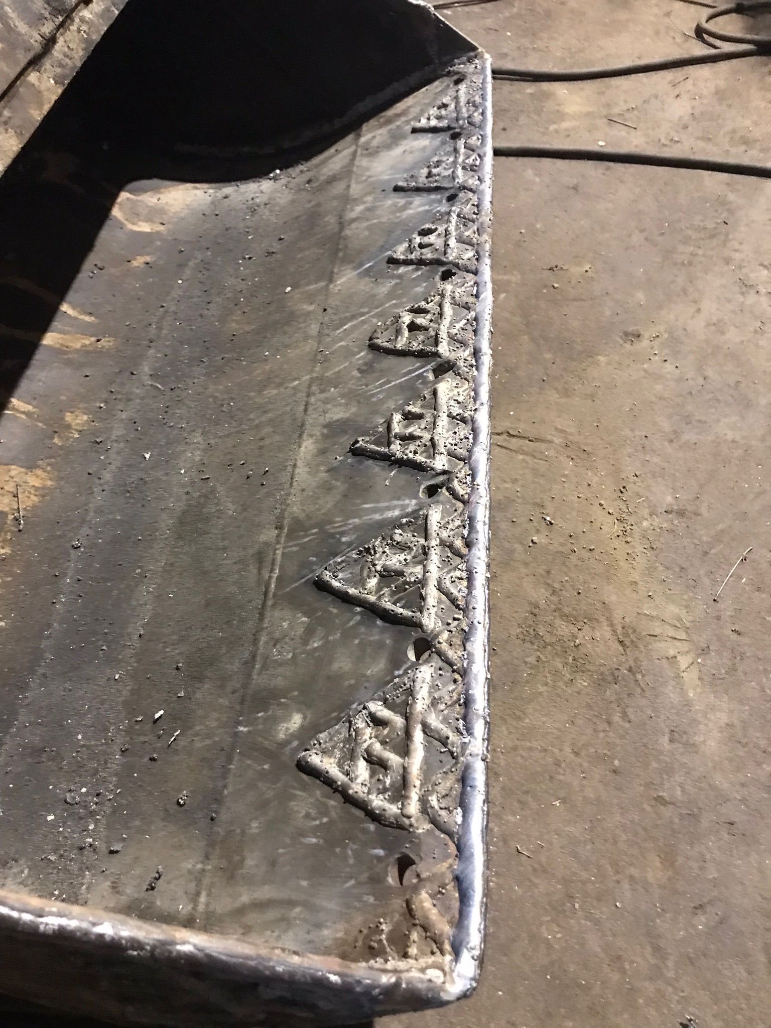 Close-up of a worn metal blade with triangular welds along the edge on a concrete floor