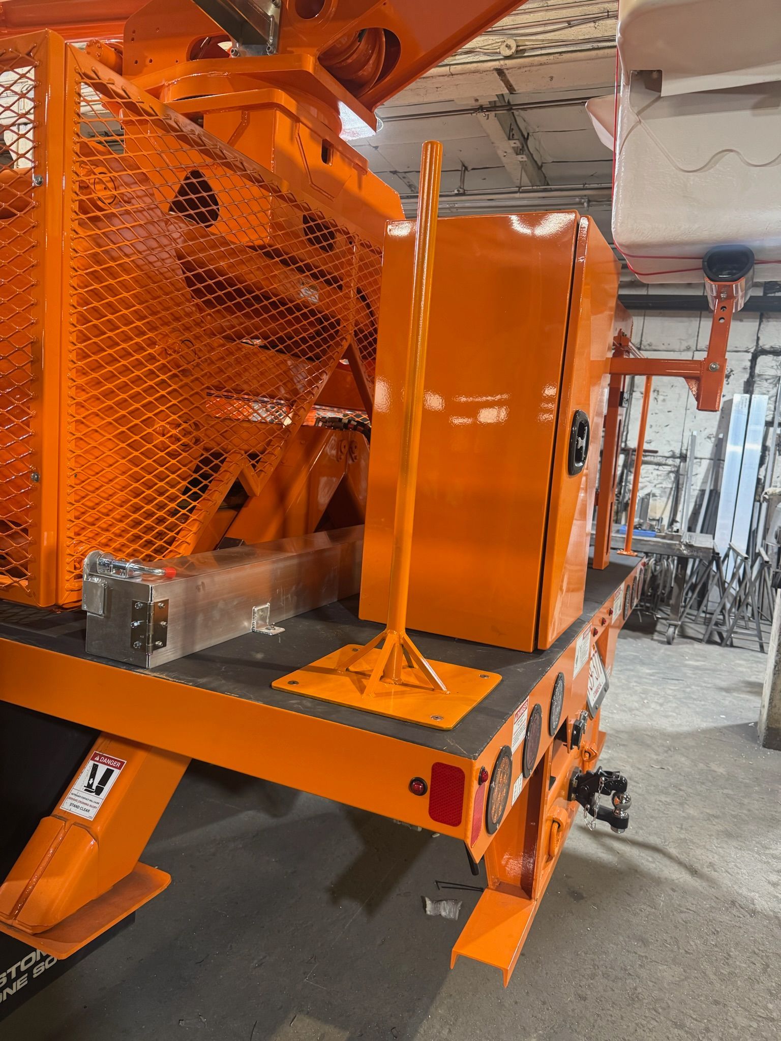 Orange industrial machine with metal mesh guard on a factory floor.